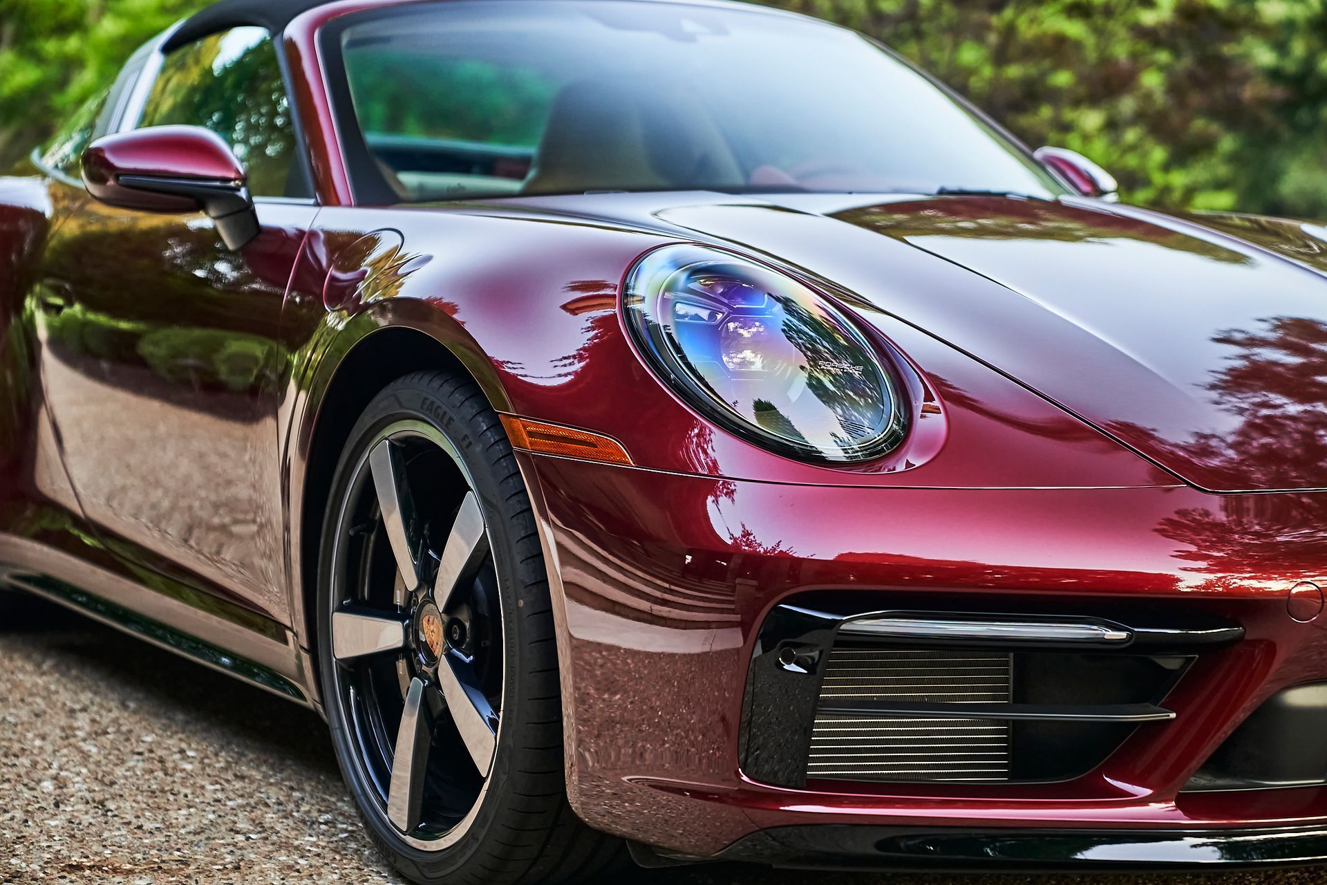 A red sports car is parked on a gravel road.