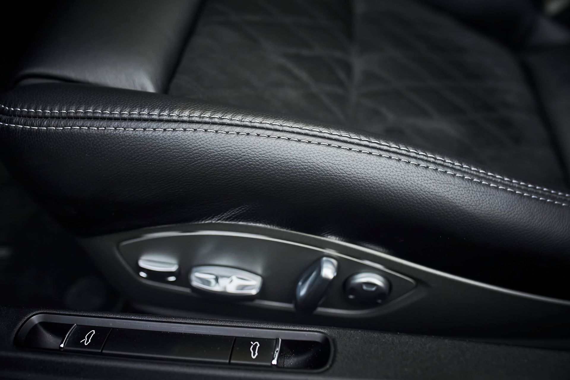 Black leather car seat with white stitching and seat adjustment controls.