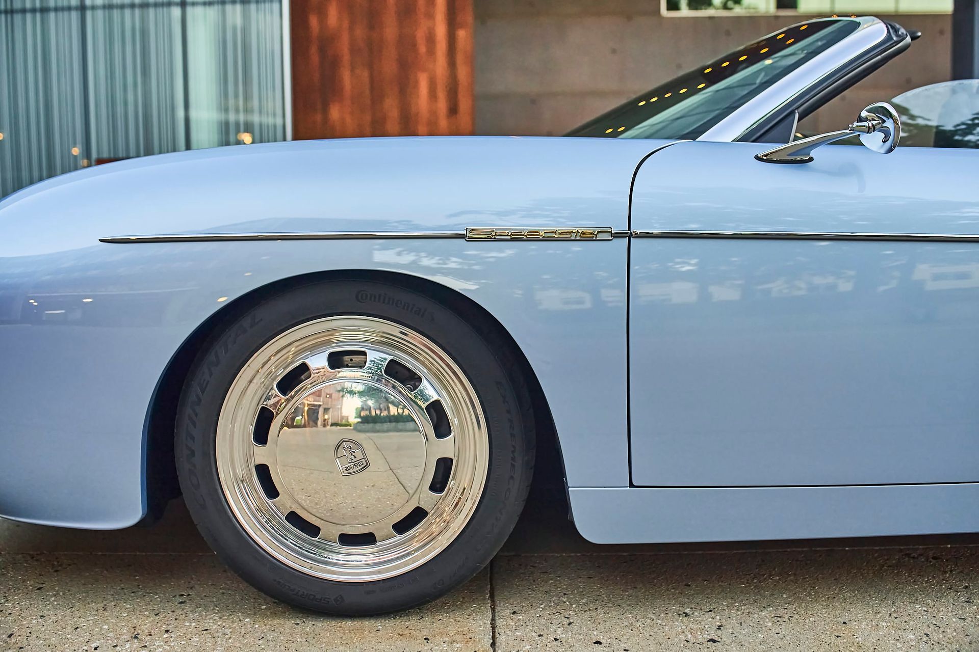 Light blue vintage convertible car with chrome wheel against a building.