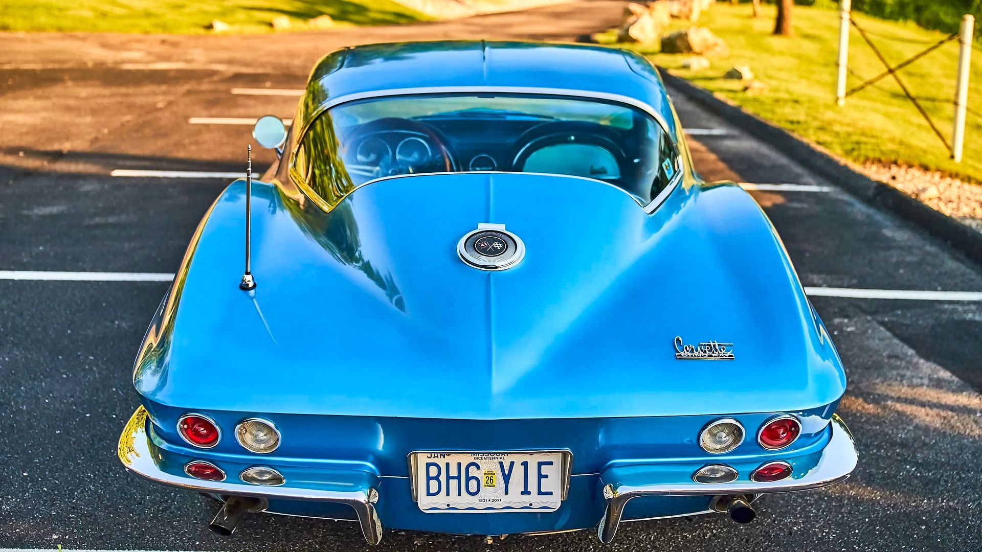 Blue vintage Corvette coupe parked outdoors, rear view. Bright blue paint, chrome accents, and license plate visible.