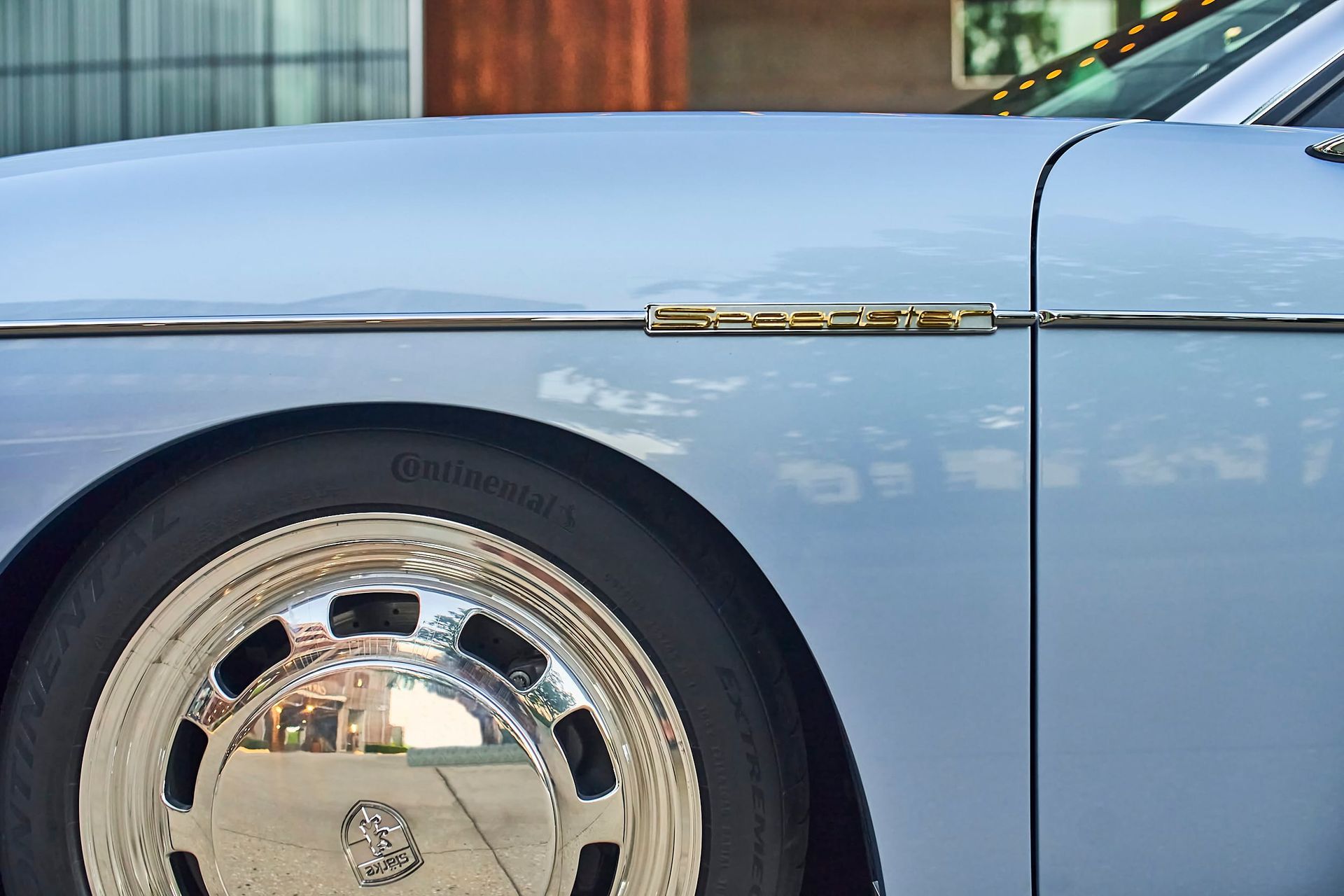 Close-up of a light blue vintage car's front quarter panel with chrome accents, a shiny hubcap, and a Continental tire.
