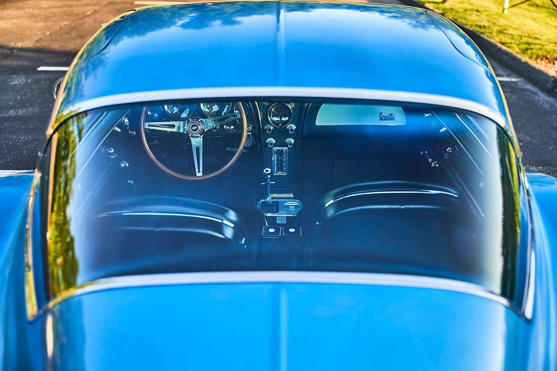 Blue classic car's interior seen through the windshield. Wooden steering wheel and dashboard visible.
