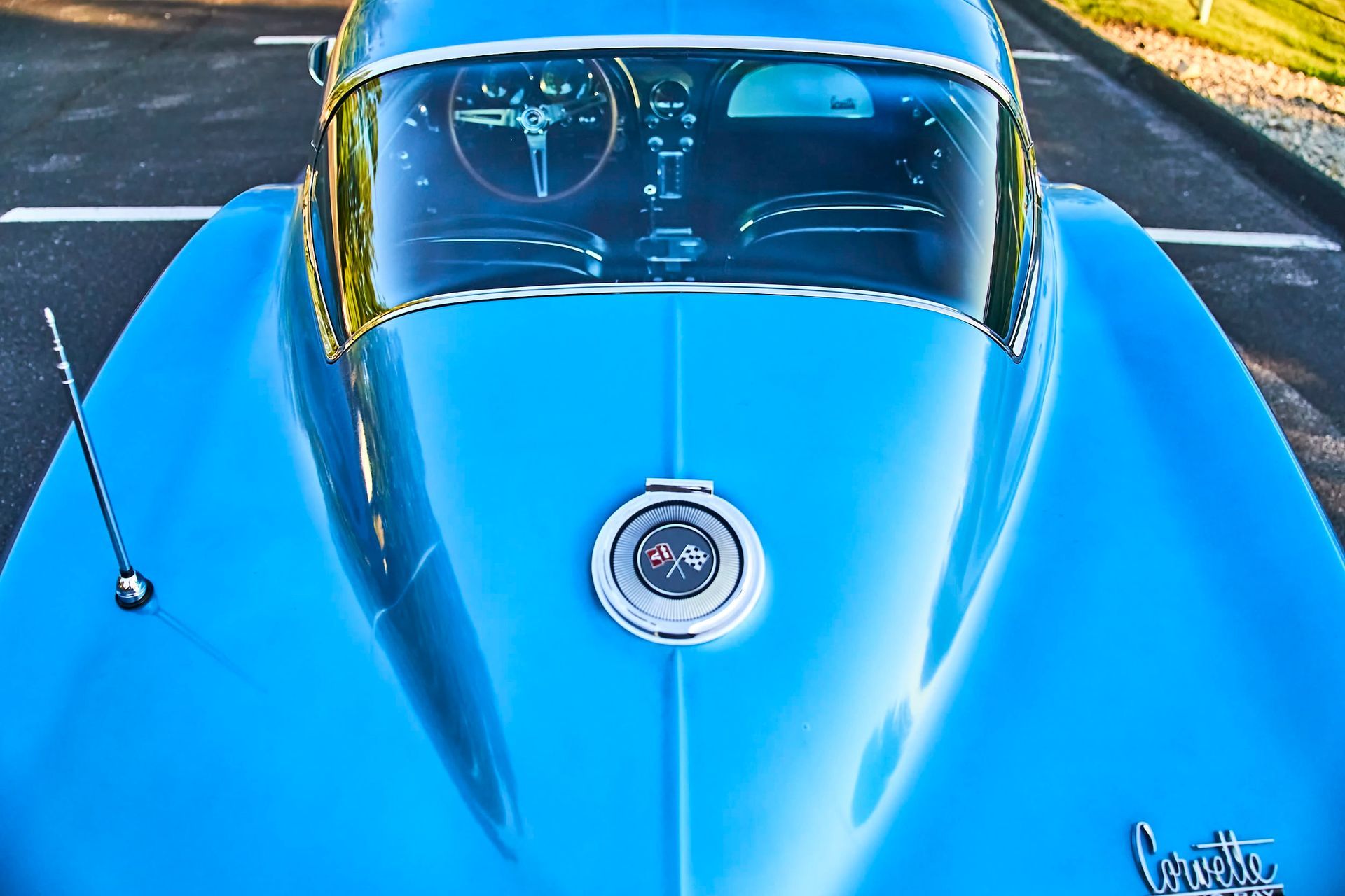 Blue classic Corvette from a top-down perspective, showing hood emblem and windshield. The car is parked outdoors.