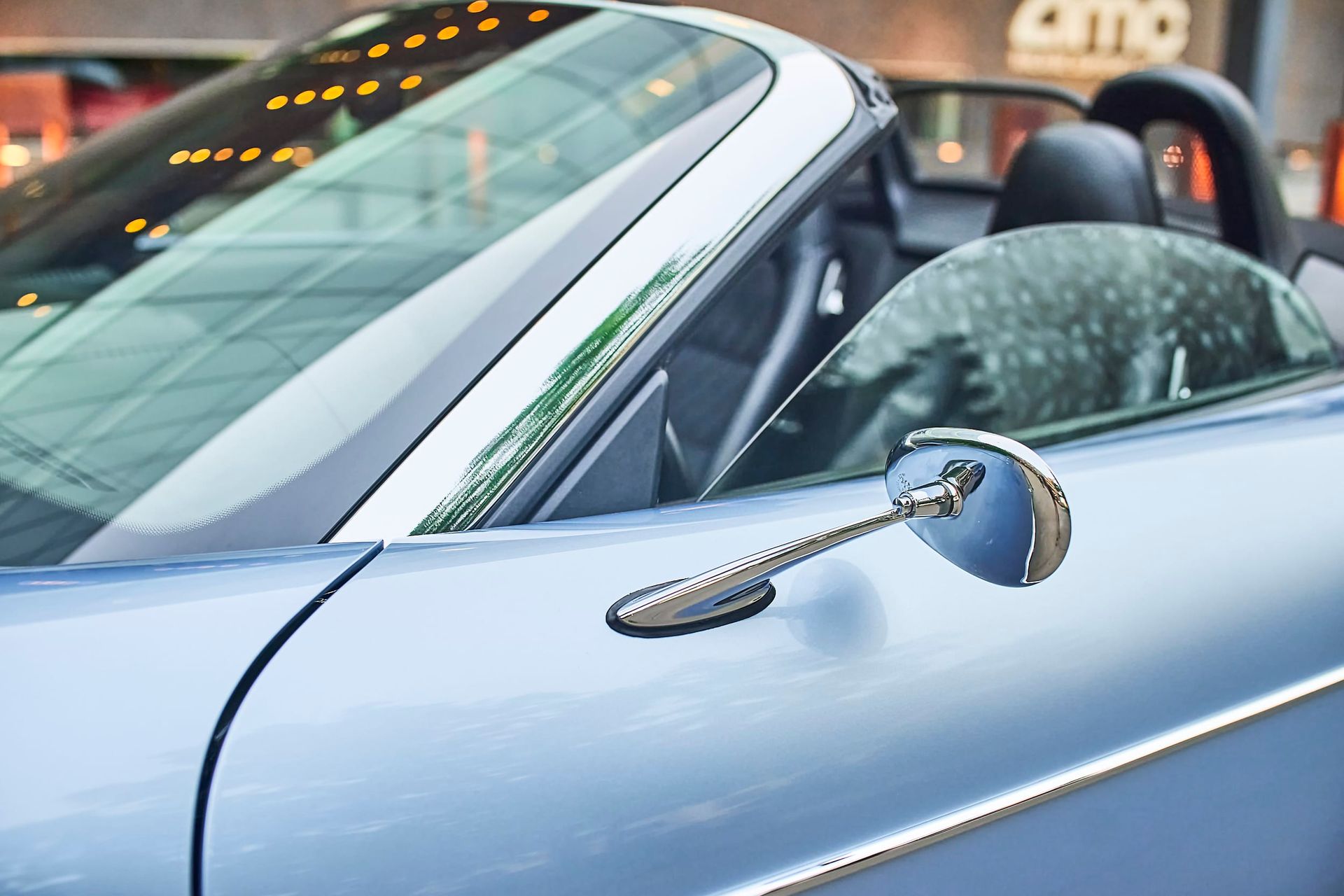 Blue convertible sports car, close-up of side mirror and windshield reflecting a building, parked outdoors.