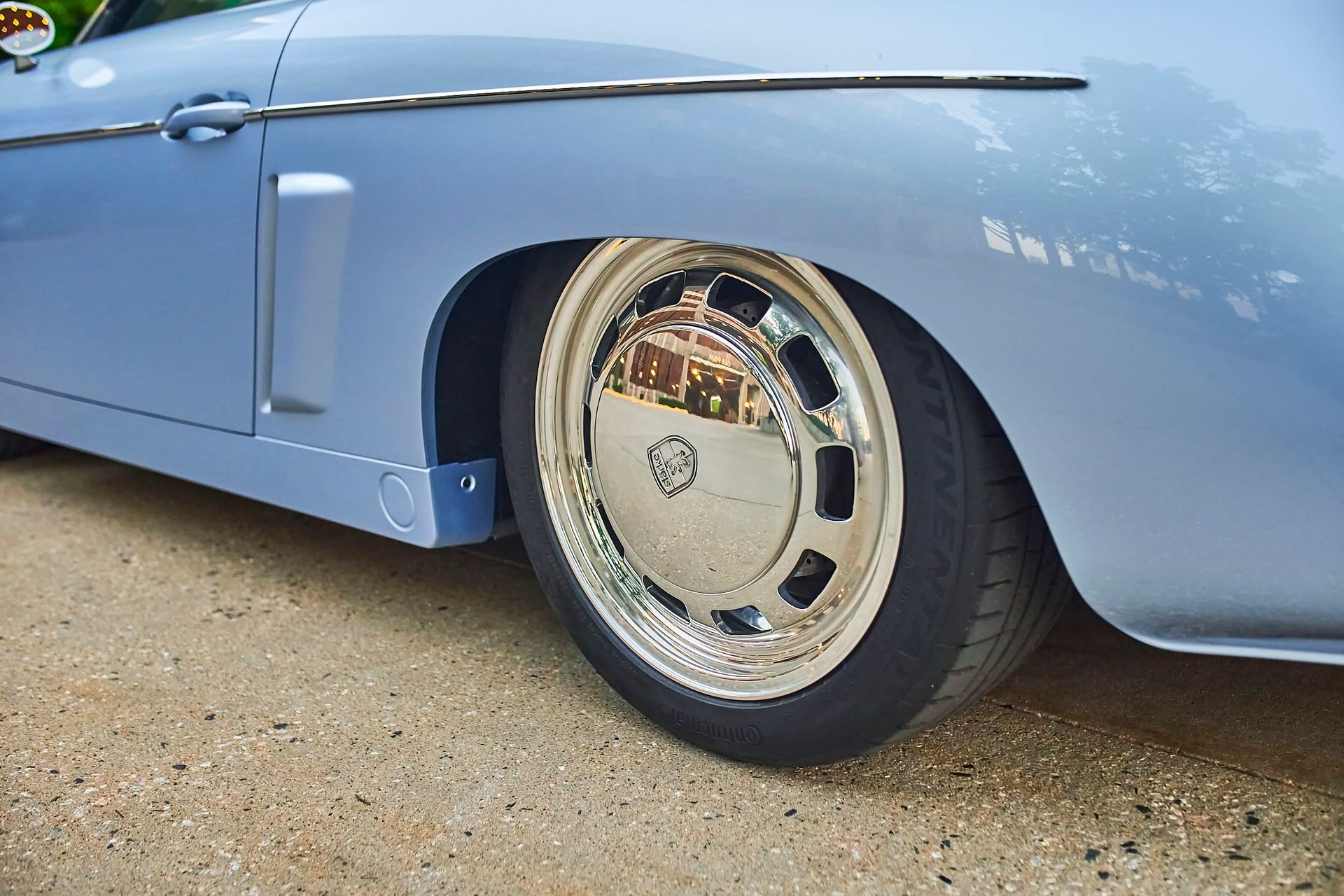 Close-up of a light blue classic car's wheel with a chrome hubcap, reflecting the surrounding environment.