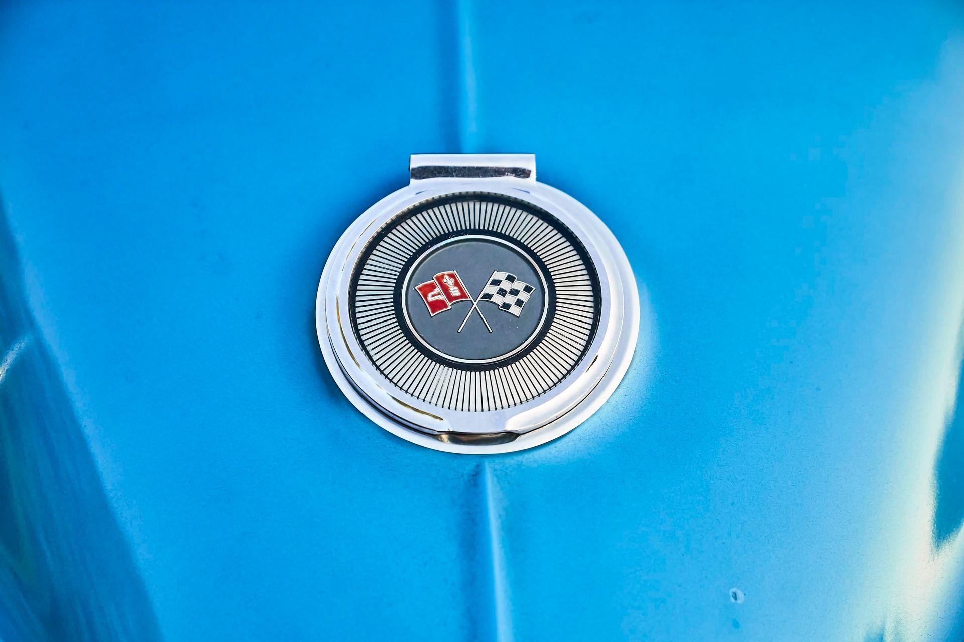 Chrome emblem with red and checkered flags on a bright blue car hood.