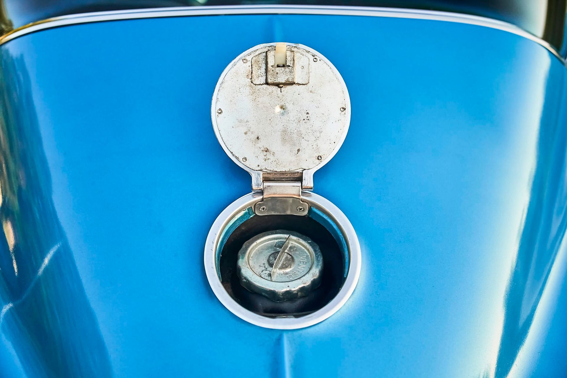 Open fuel tank door on a blue car, revealing the gas cap within a silver-colored rim.
