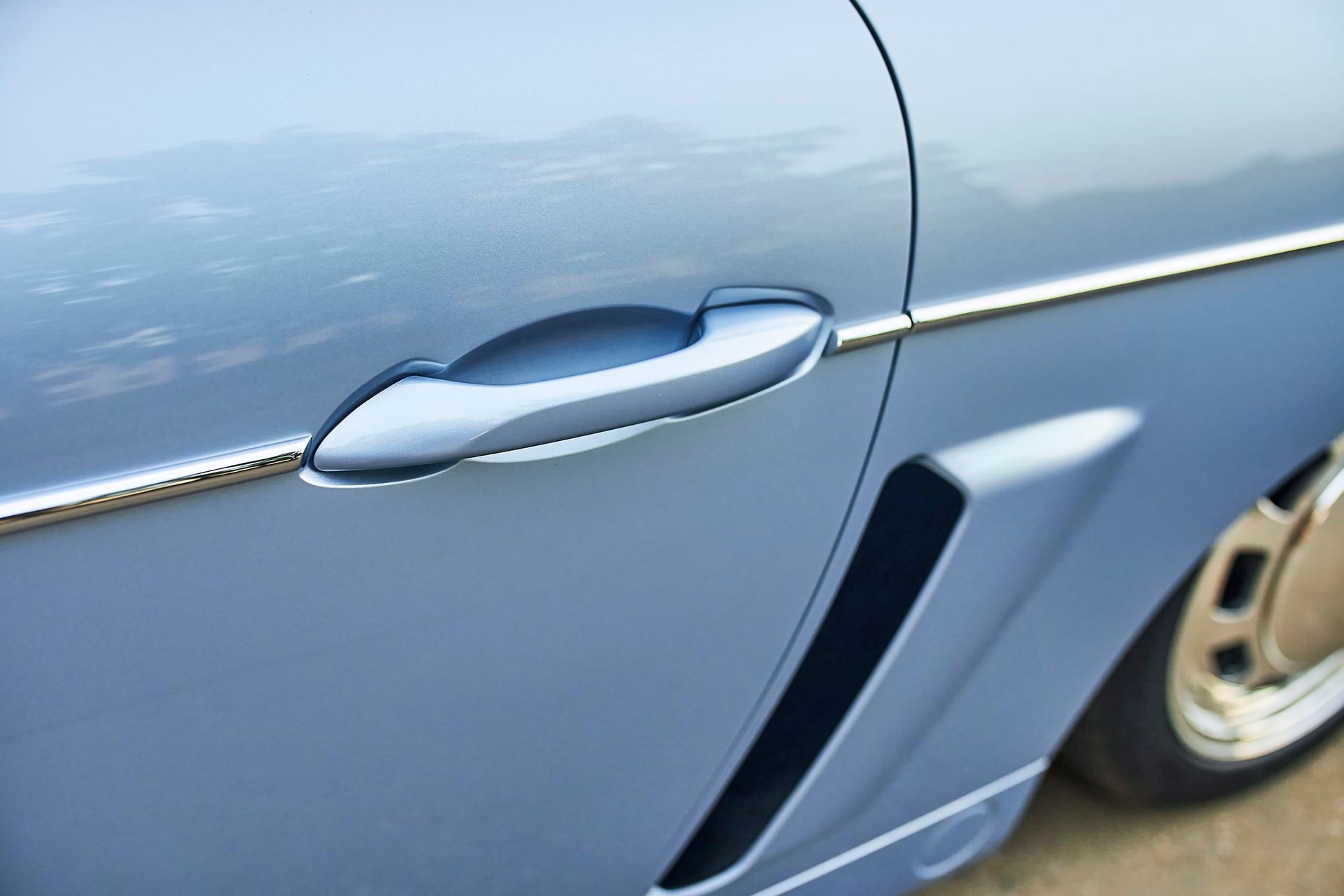 Light blue car door with a silver handle and trim, part of a wheel is visible.