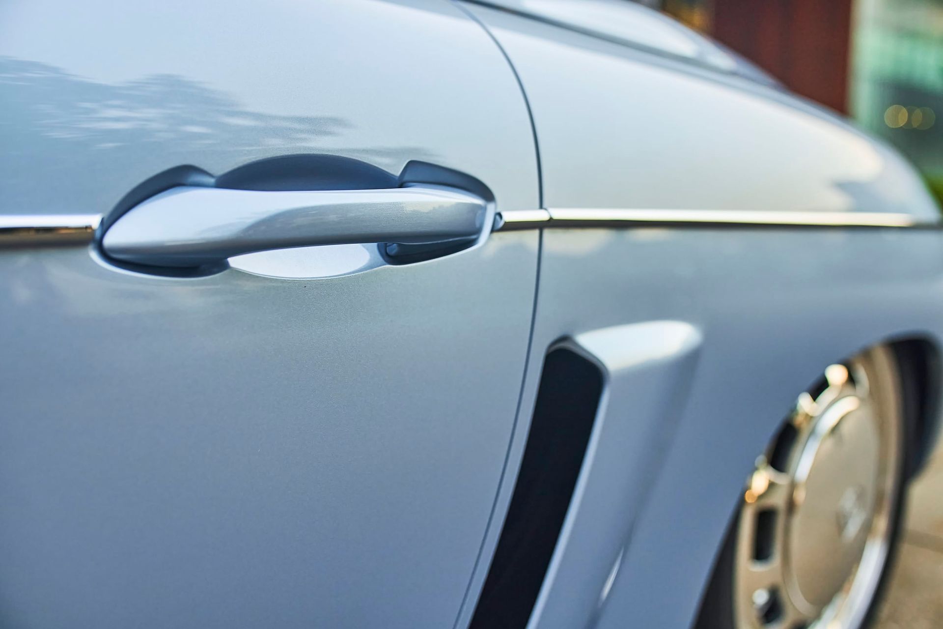 Close-up of a light blue vintage car's side, showing the door handle, chrome trim, and a vent.