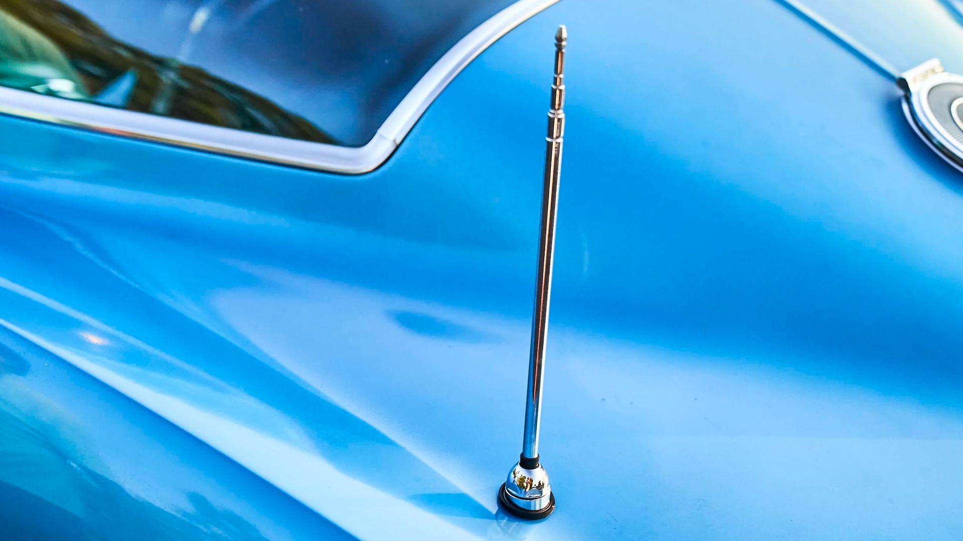 Chrome antenna on a light blue classic car hood. Close-up view.