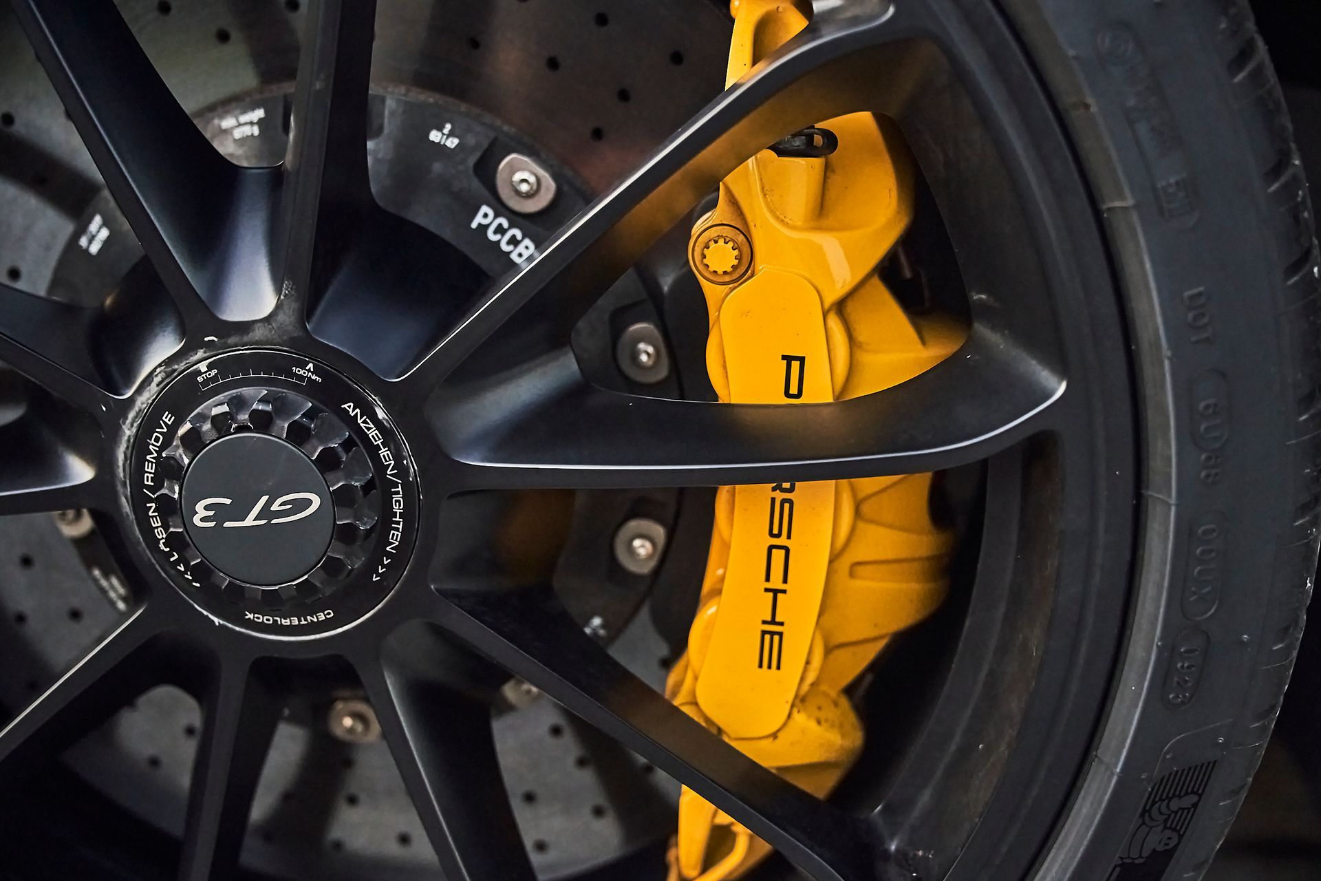 A close up of a porsche wheel with yellow brake calipers