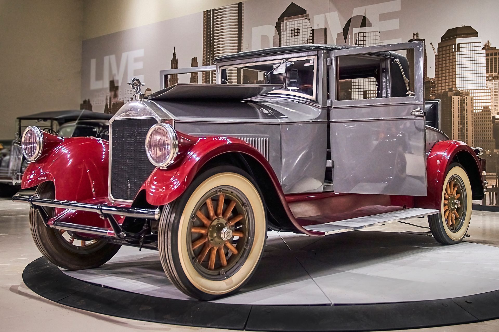 An old car is on display in front of a wall that says live