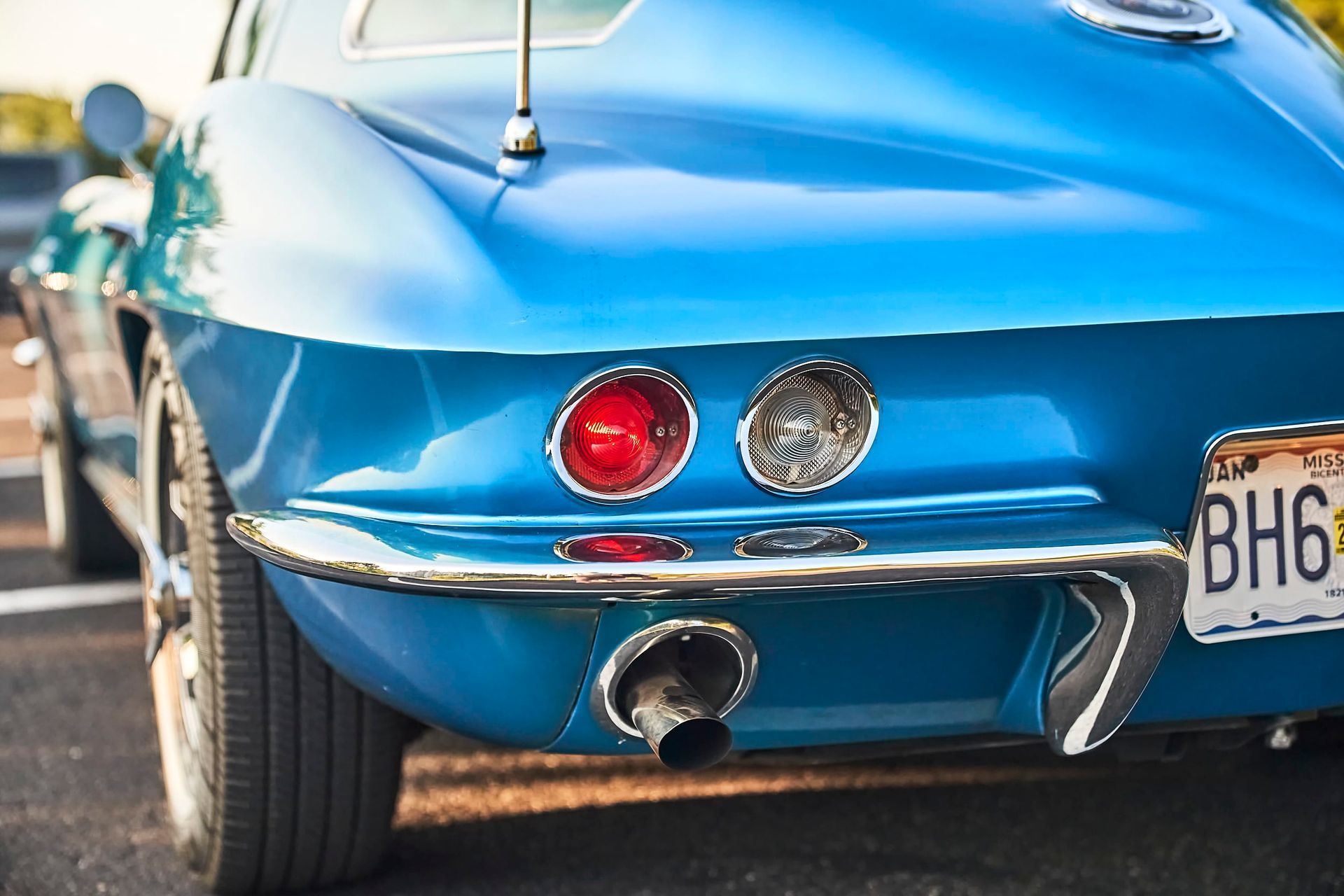 Rear view of a bright blue classic Corvette sports car, showing a red tail light, chrome trim, and the exhaust pipe.