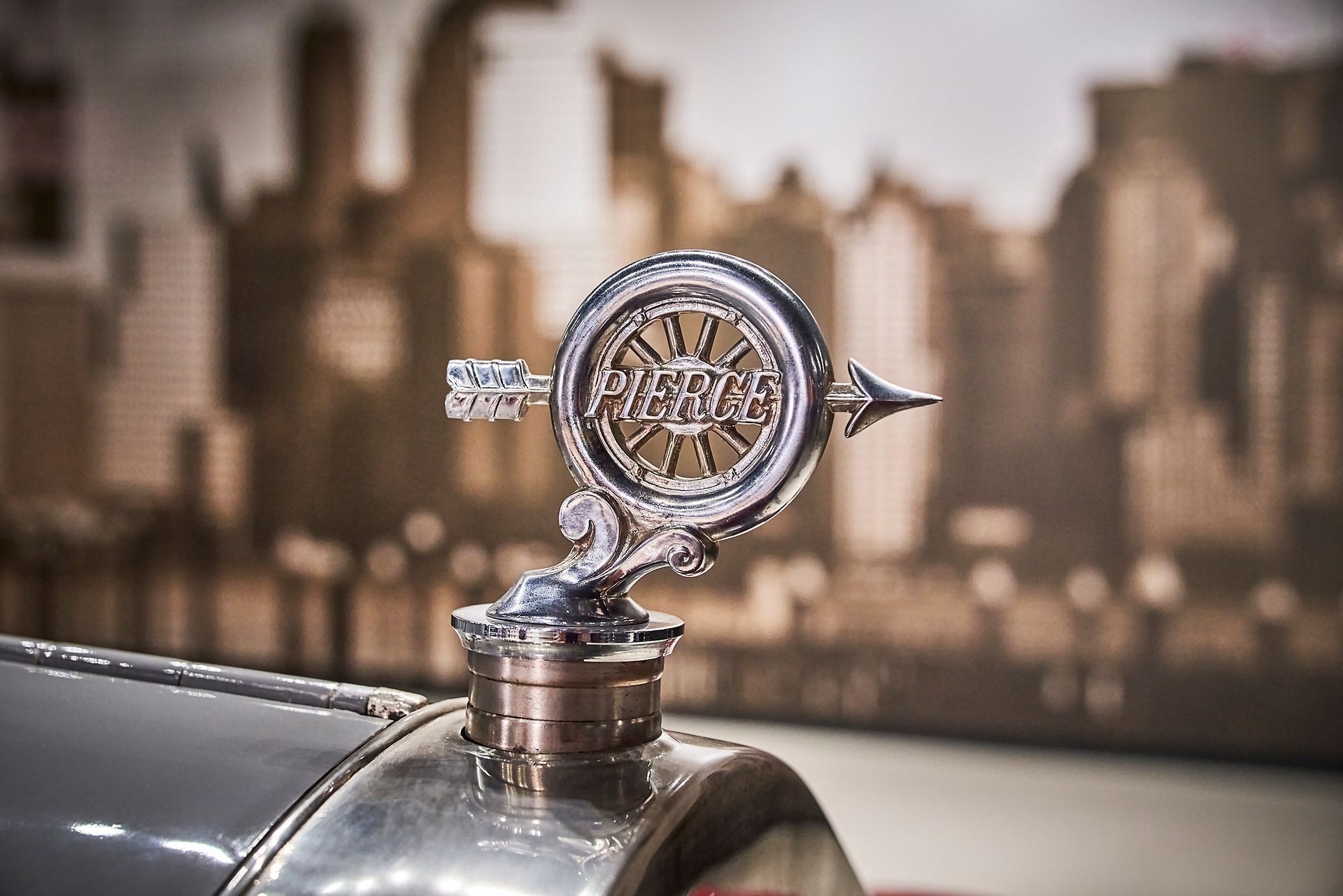 A close up of a car hood ornament with a city in the background