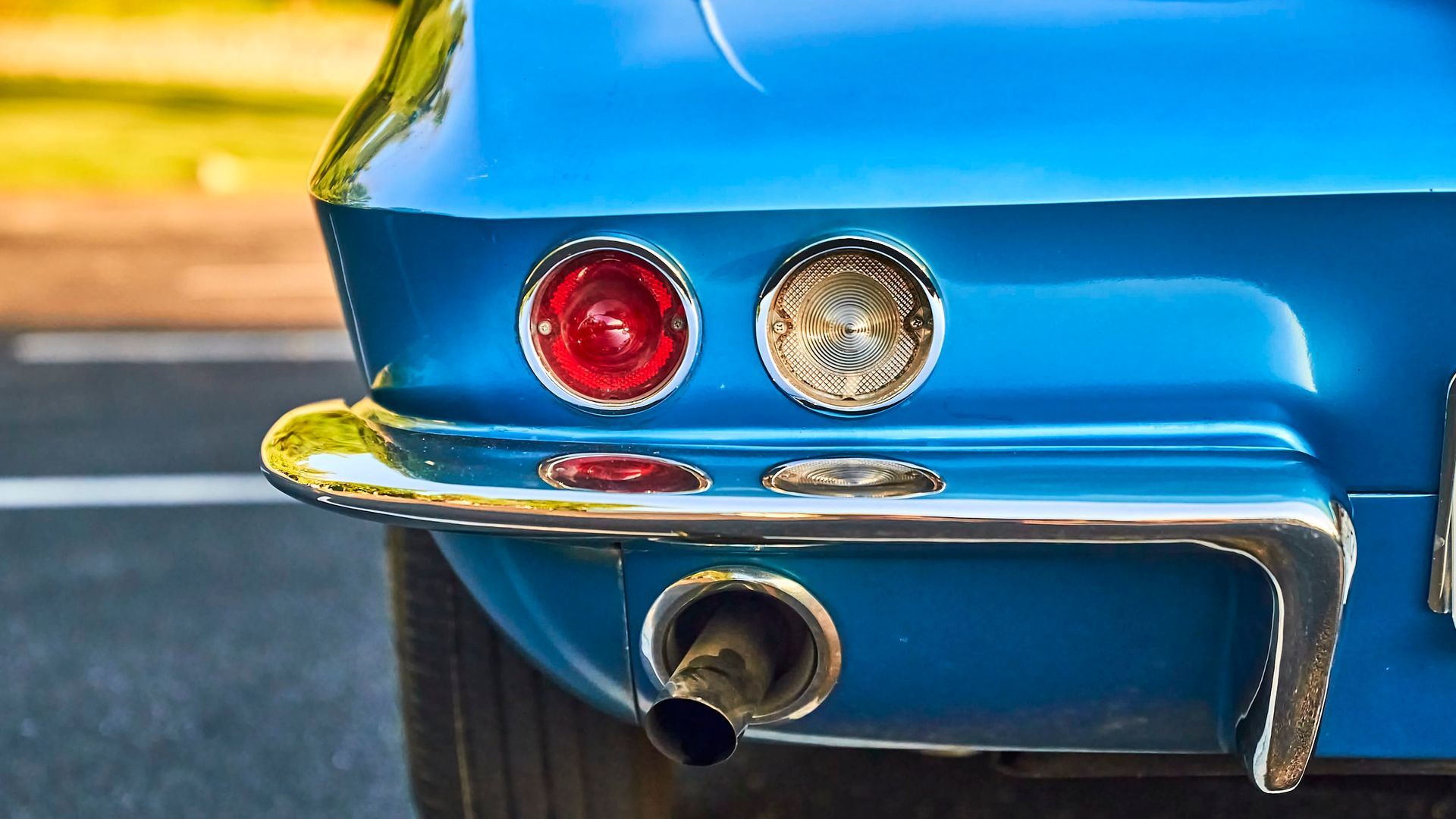Close-up of the rear end of a classic blue car with chrome accents, exhaust pipe, and round red and white tail lights.