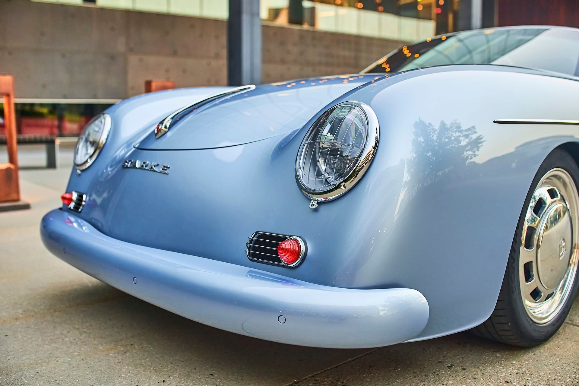 Close-up of a vintage light blue Porsche 356, parked on a sidewalk in front of a building.