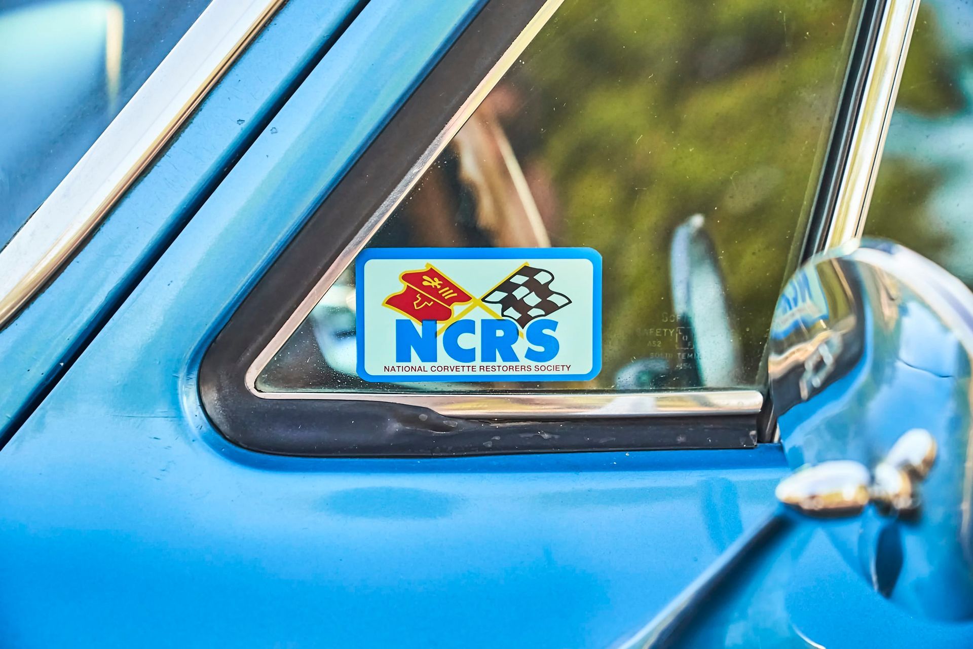 Blue car window with a sticker that reads 