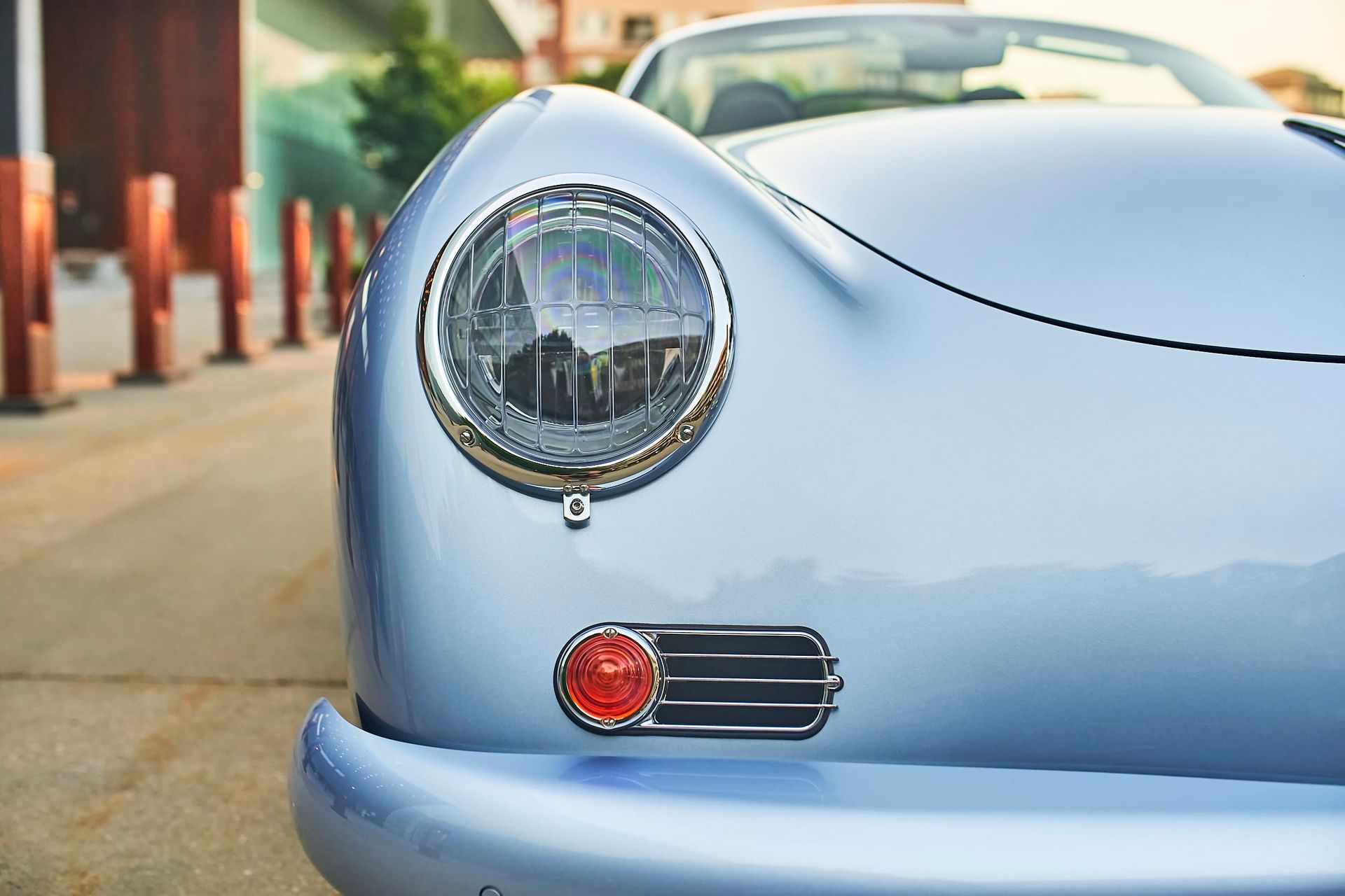 Close-up of a light blue vintage Porsche car's front. Focus on the headlight and side marker light, with a blurred background.
