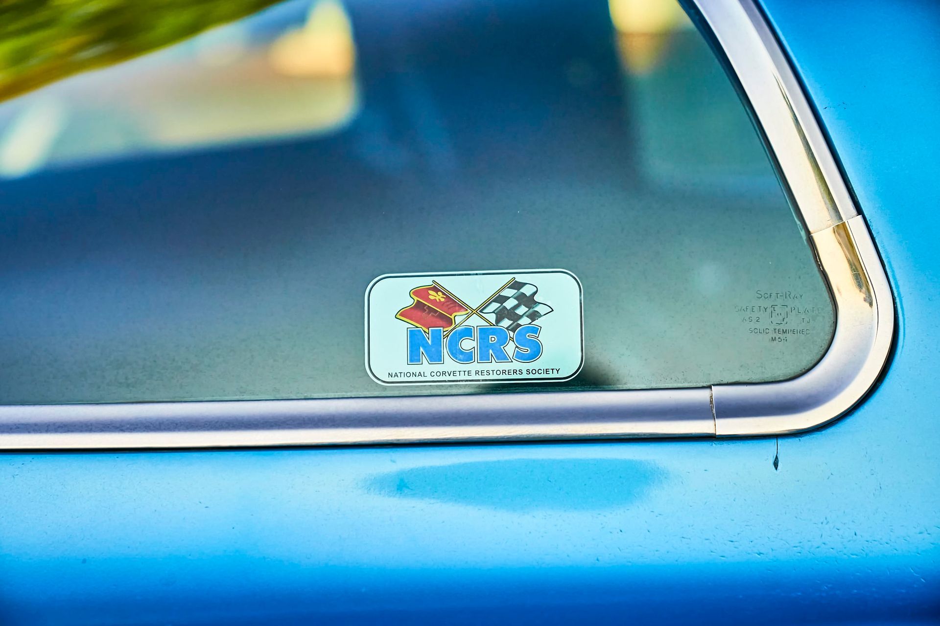 Close-up of a blue car window with an NCRS (National Corvette Restorers Society) sticker visible.