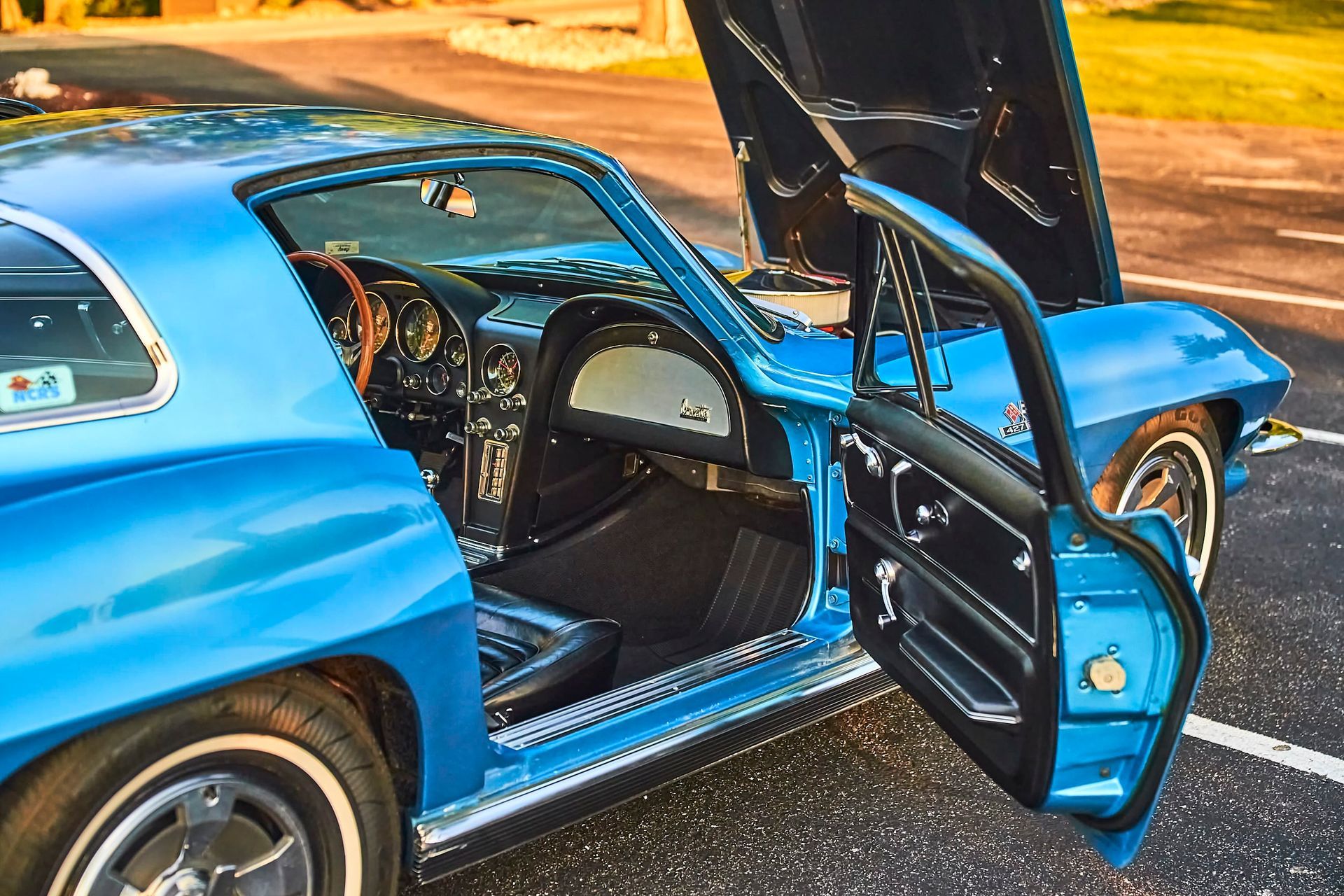 Blue classic Corvette with the door and hood open, parked outside on a sunny day. The interior is black and tan.