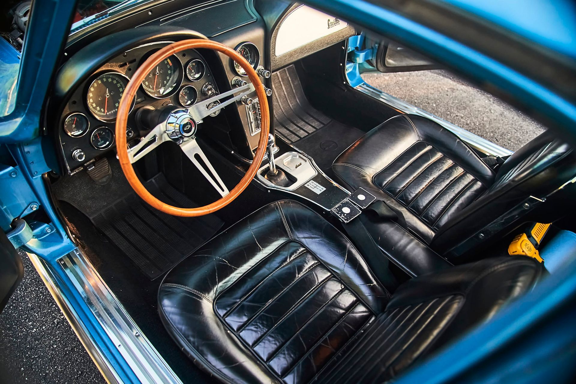 Interior view of a vintage blue sports car with black leather seats, wood steering wheel, and chrome details.