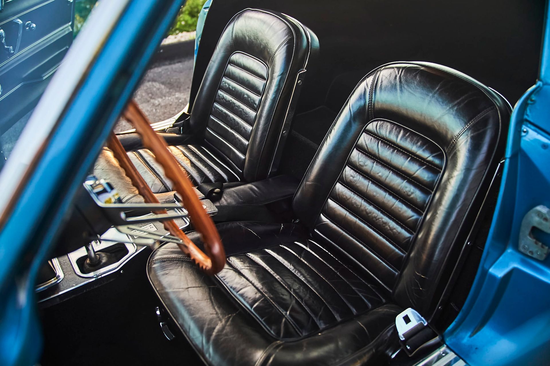 Blue car interior with black leather bucket seats and a wooden steering wheel.