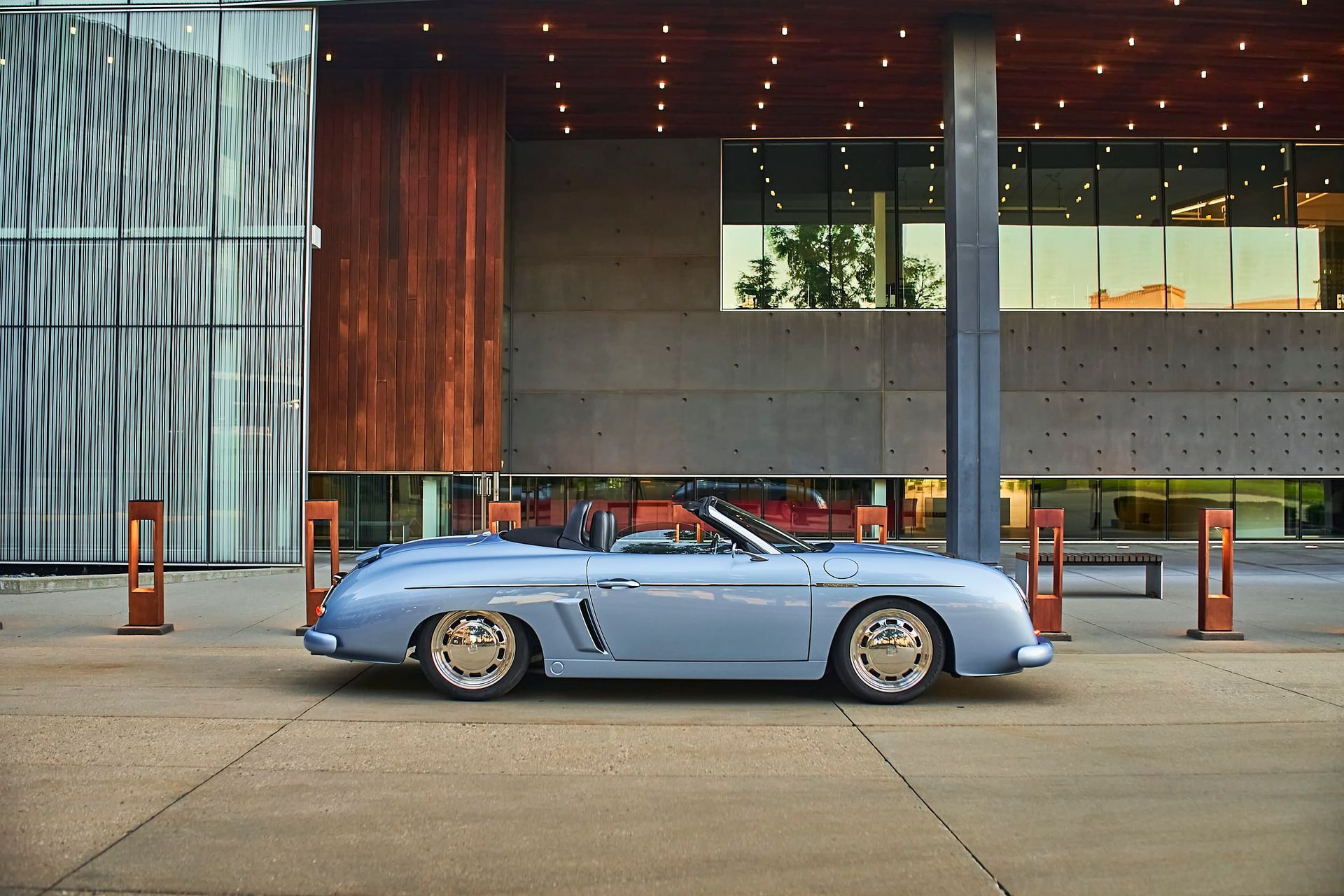 Light blue convertible parked in front of a modern building with a brown and concrete facade.