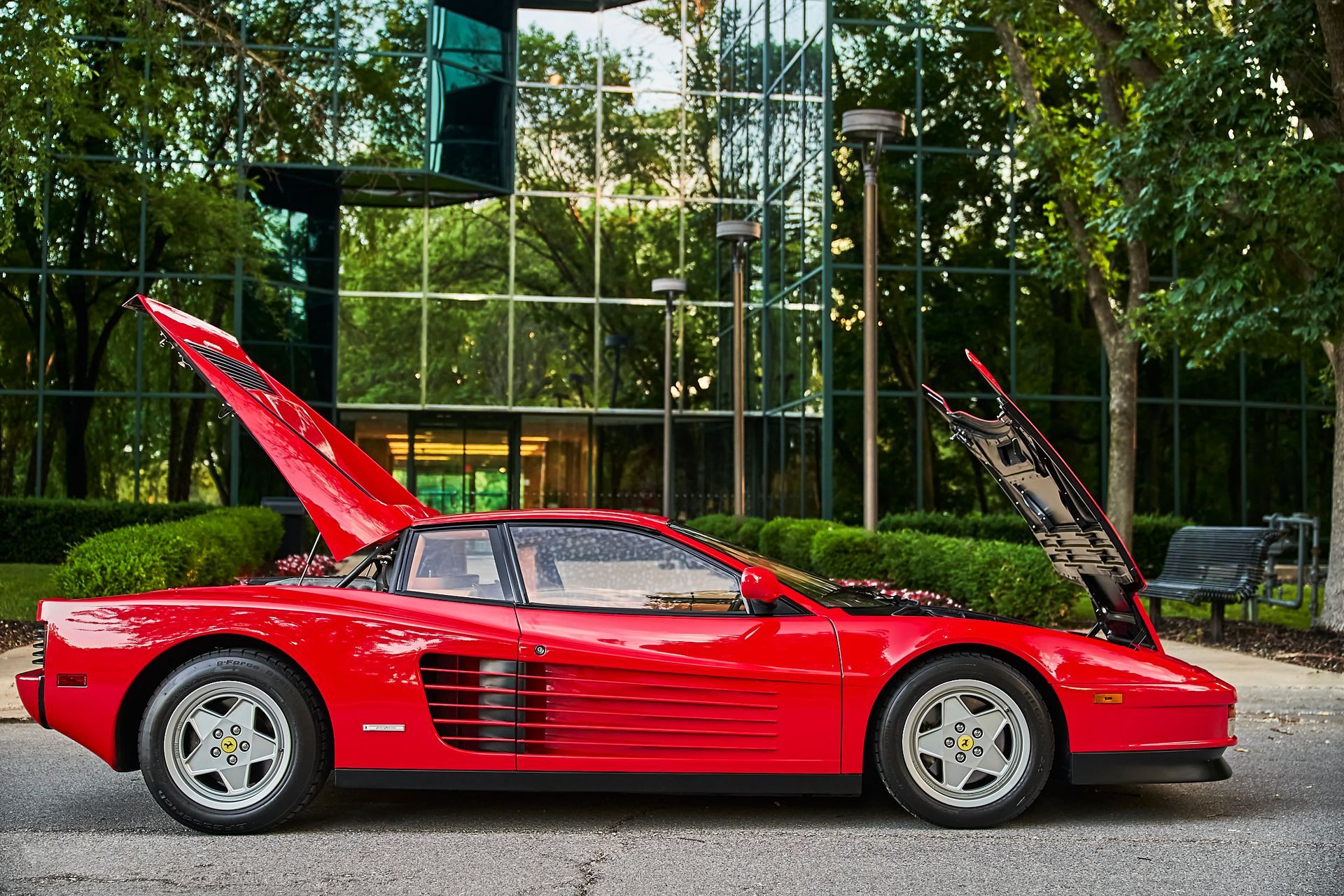 A red ferrari testarossa with its hood up is parked in front of a building.