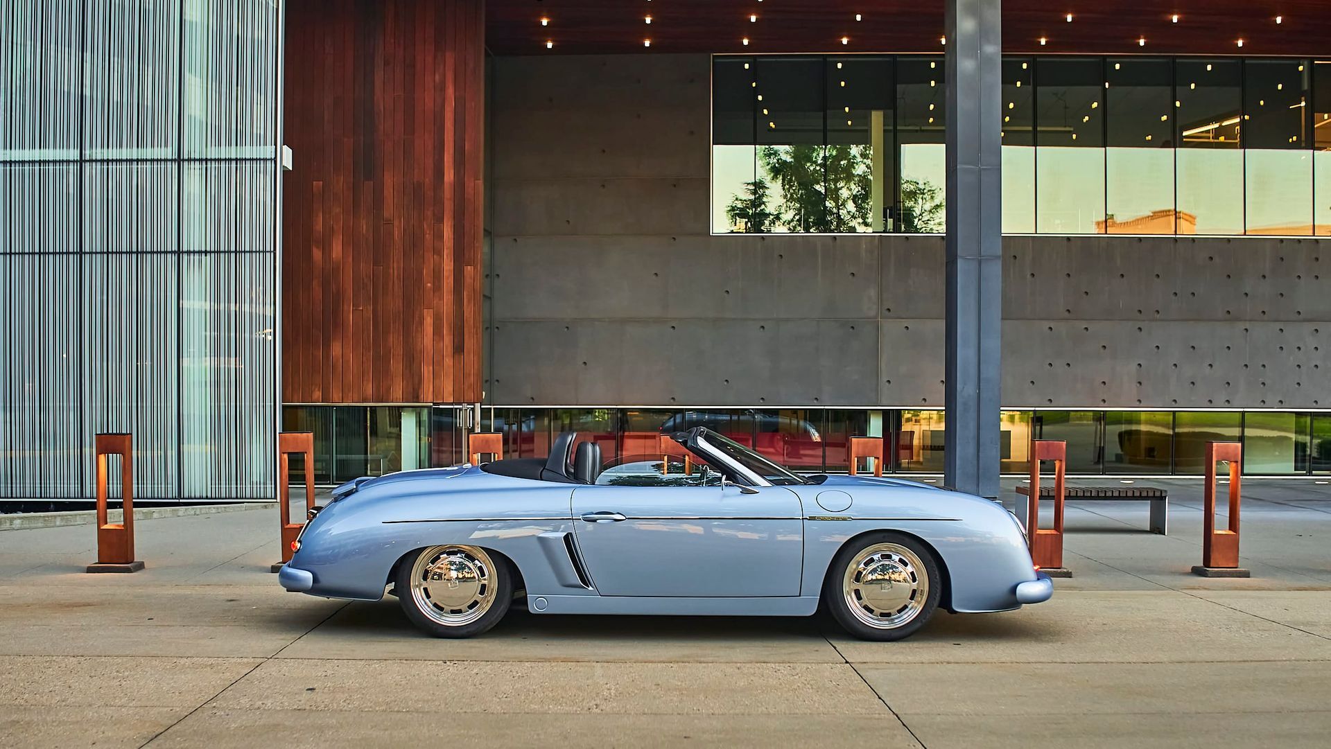 Light blue convertible car parked outside a modern building. The car has gold rims and a classic design.