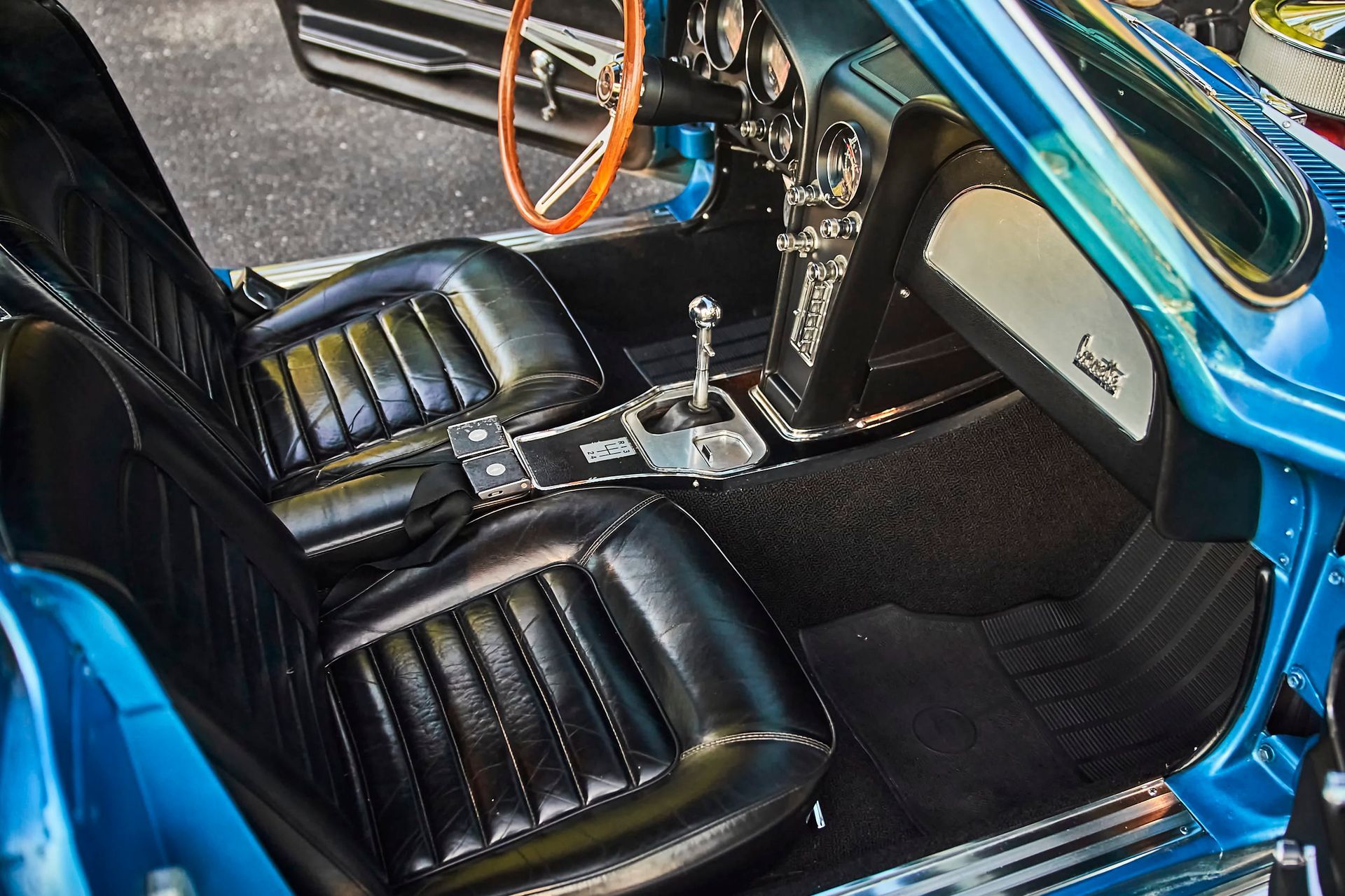 Interior of a classic blue Corvette, featuring black leather bucket seats, chrome details, and a manual transmission.