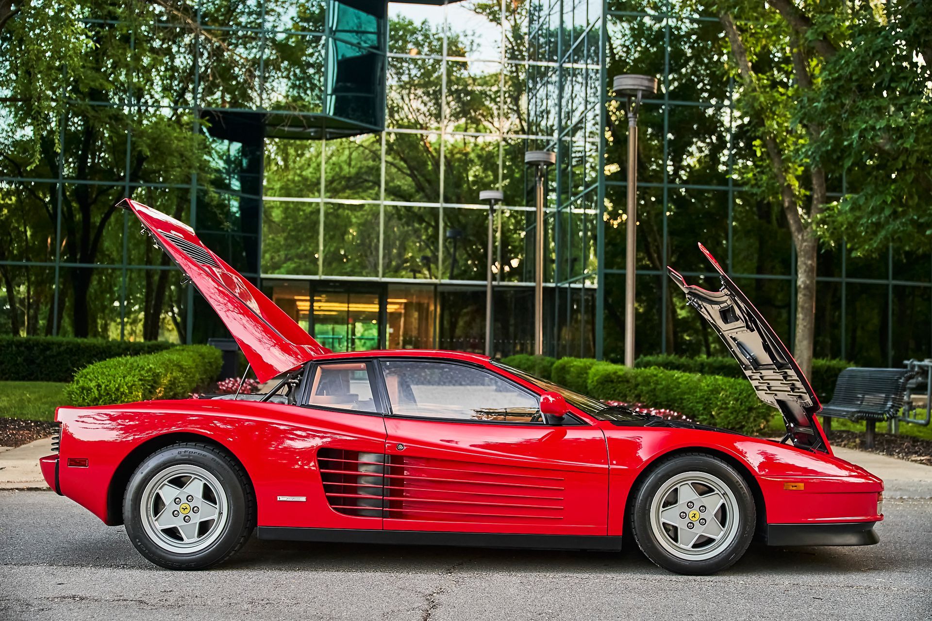 A red ferrari with the hood up is parked in front of a building.