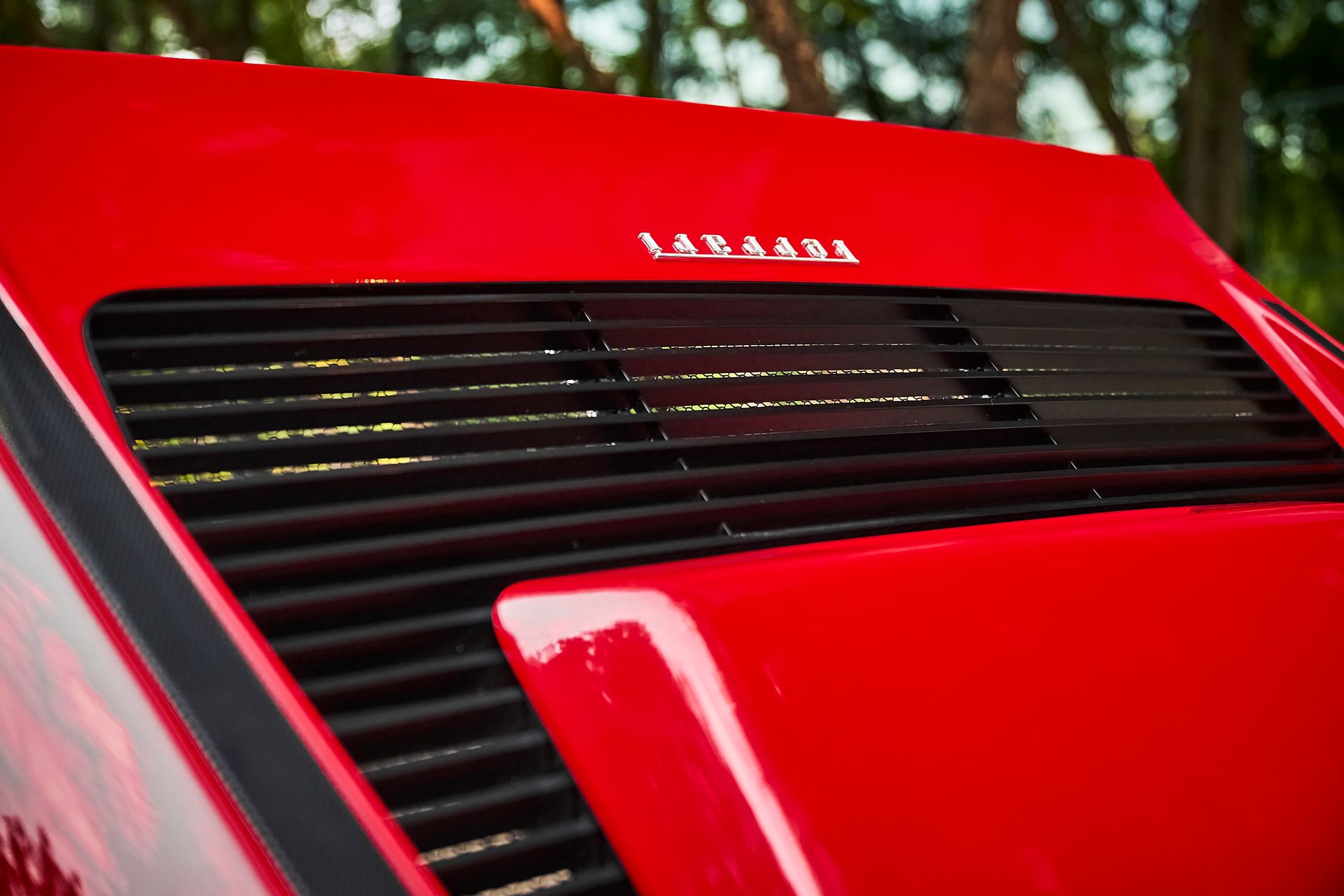 A close up of the hood of a red ferrari with trees in the background.