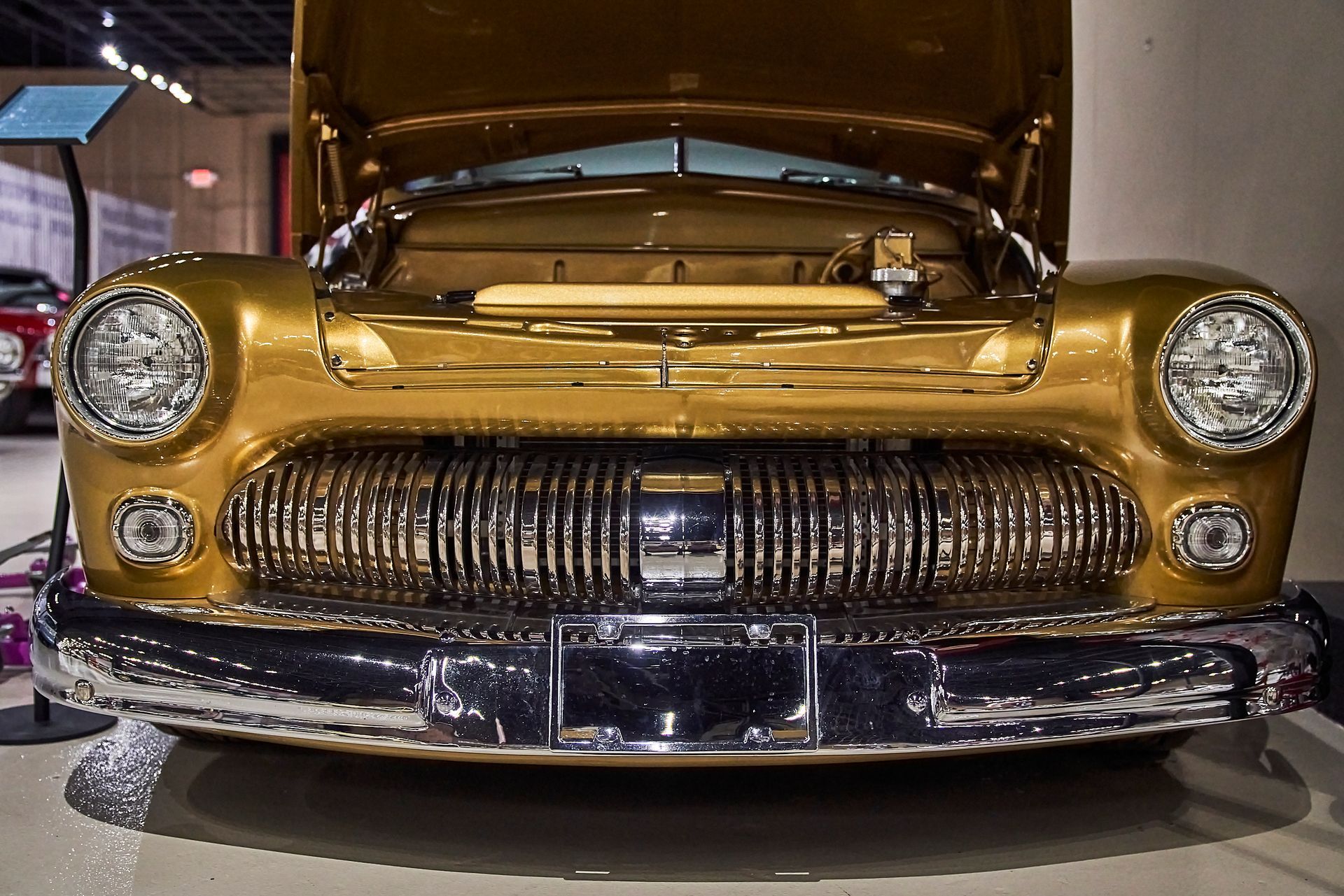 A gold car with the hood up is parked in a garage.