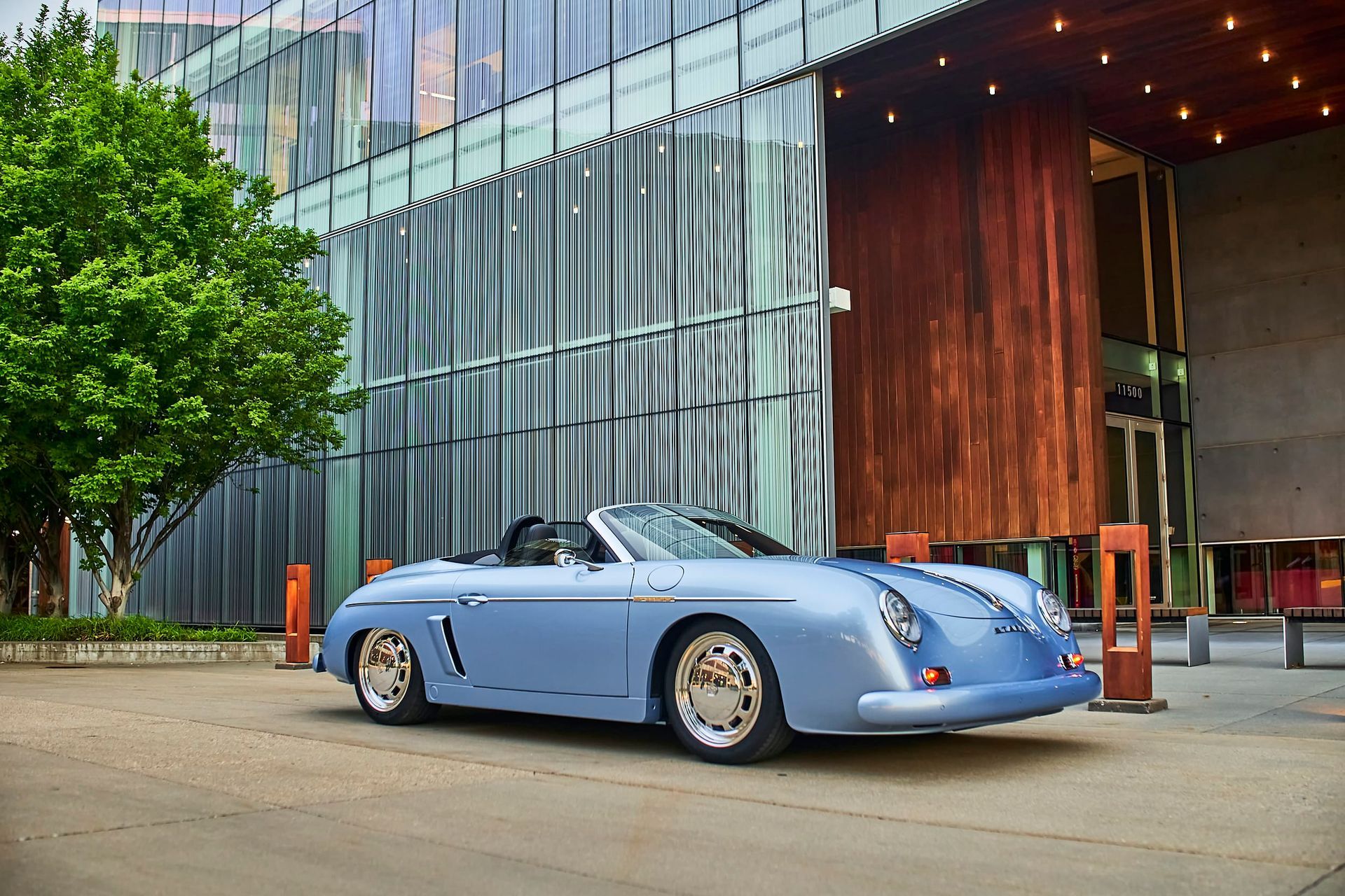 A light blue convertible sports car parked in front of a modern building with glass and wood features.