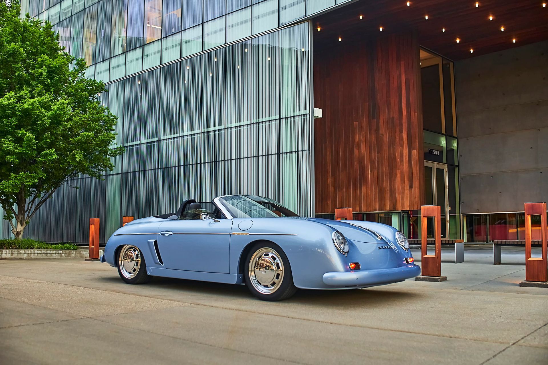 Light blue convertible car parked in front of a modern building with glass and wooden accents; sunny day.