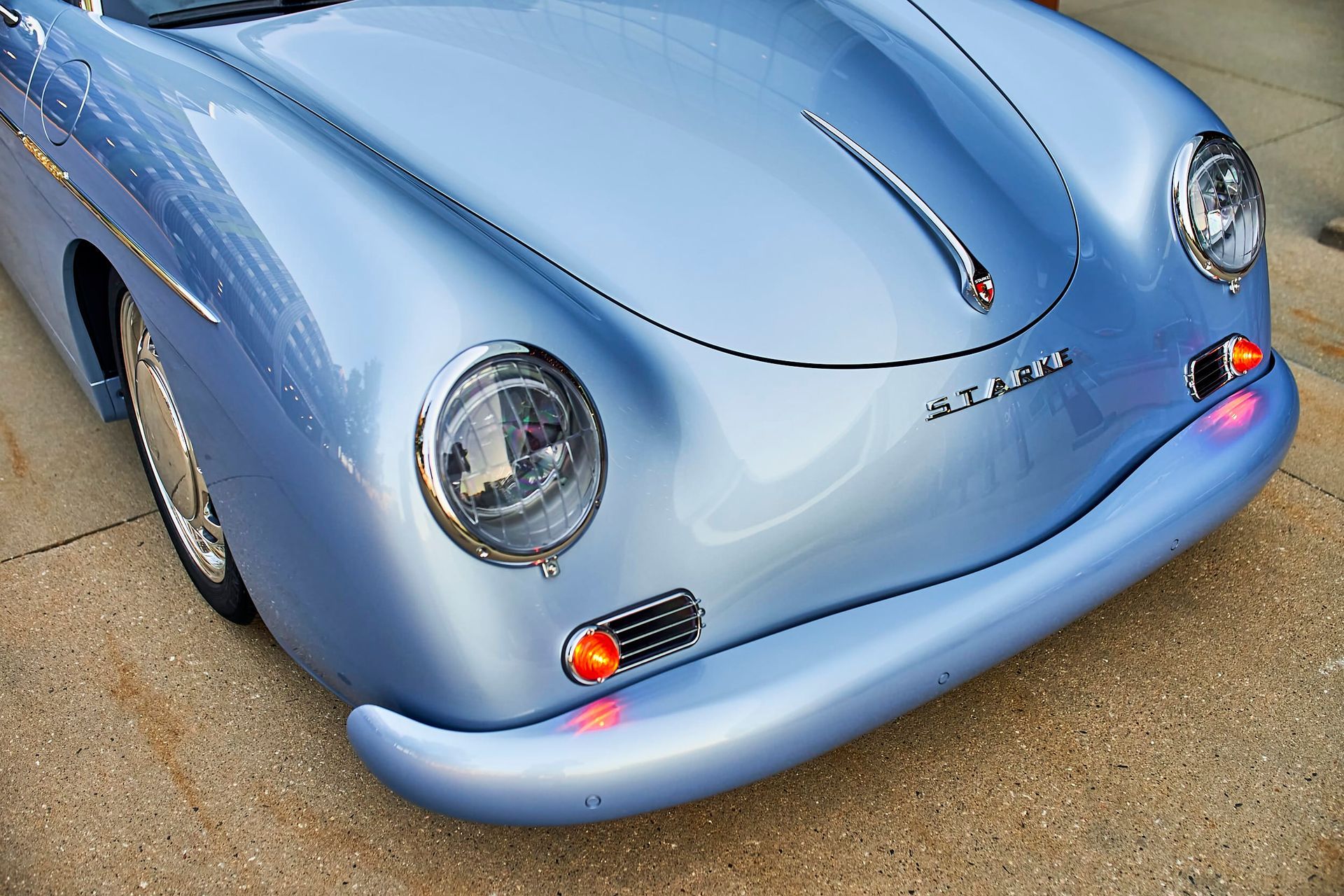Close-up of a light blue vintage Porsche sports car's front, showcasing headlights, curves, and a chrome emblem.