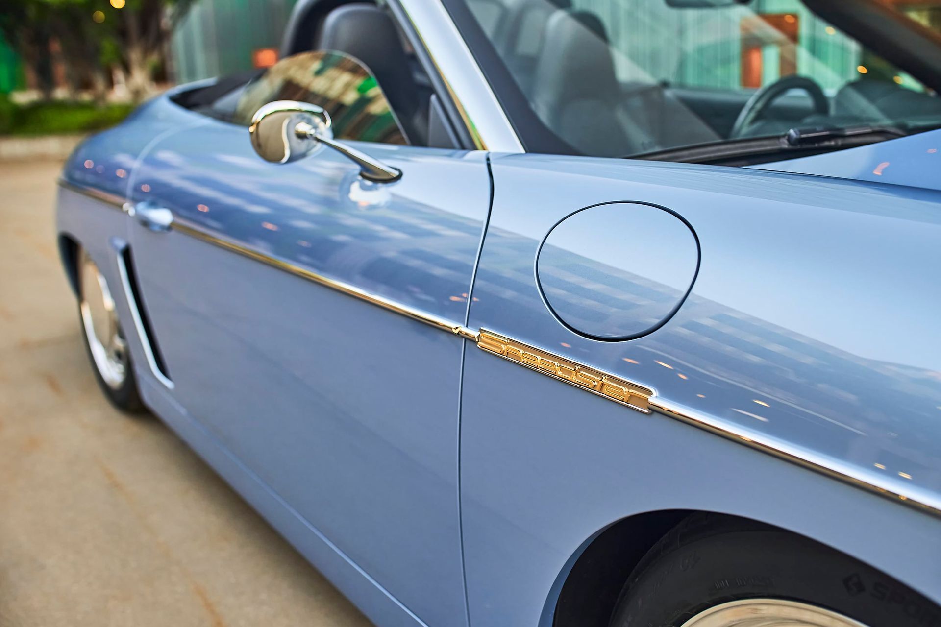 Light blue convertible car with chrome accents, showing fuel door and side mirror.