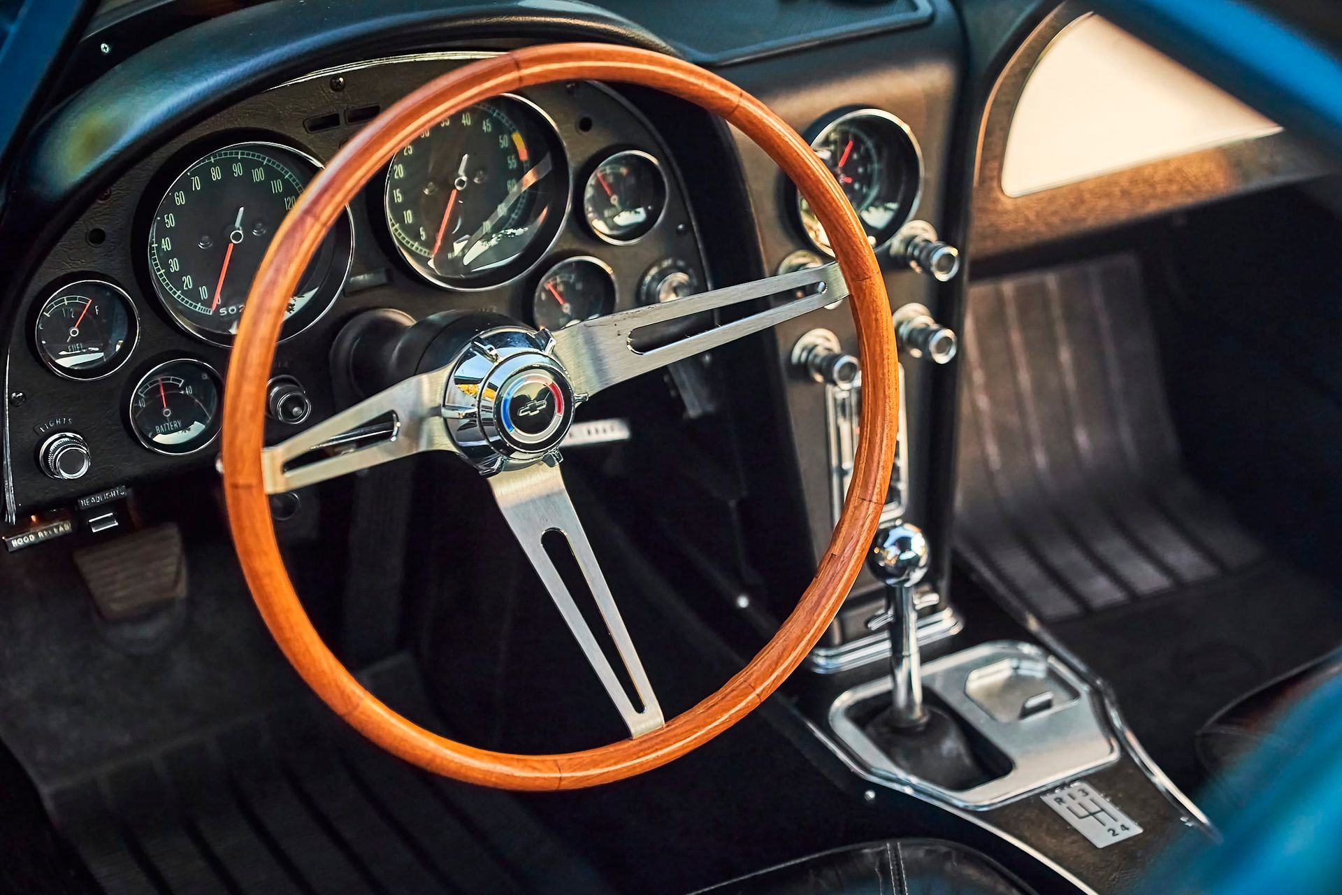 Interior of a classic car featuring a wooden steering wheel, silver gauges, and a black dashboard.