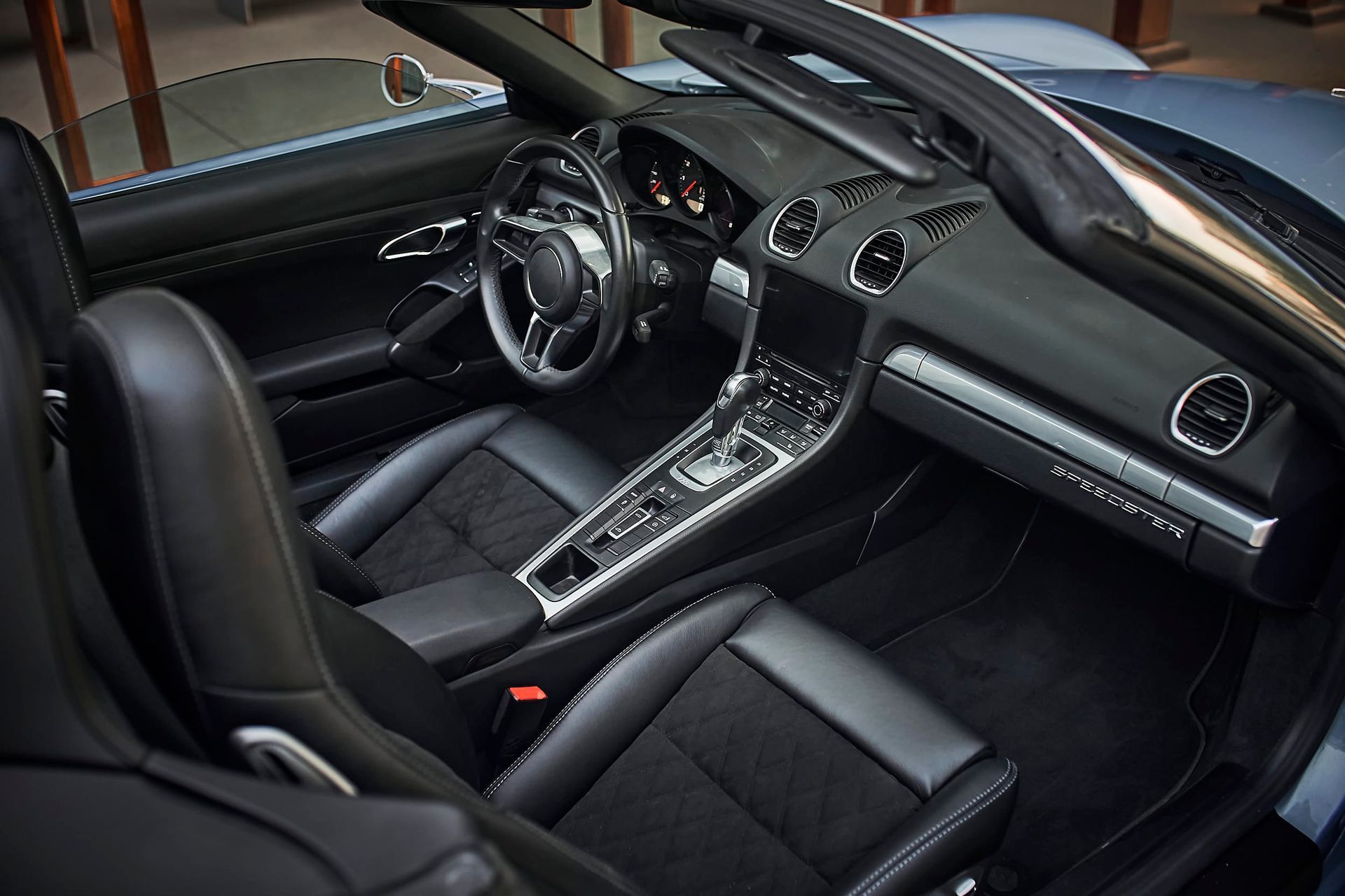 Interior of a black convertible sports car, featuring leather seats, a dashboard with controls, and a steering wheel.