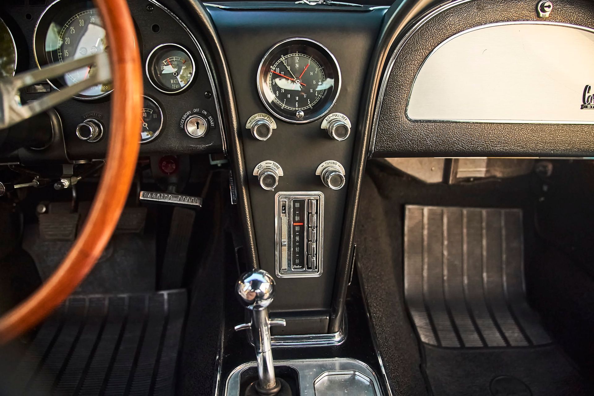 Interior of a classic black Corvette, showcasing the dashboard, steering wheel, and gear shift. The setting is likely inside the vehicle.