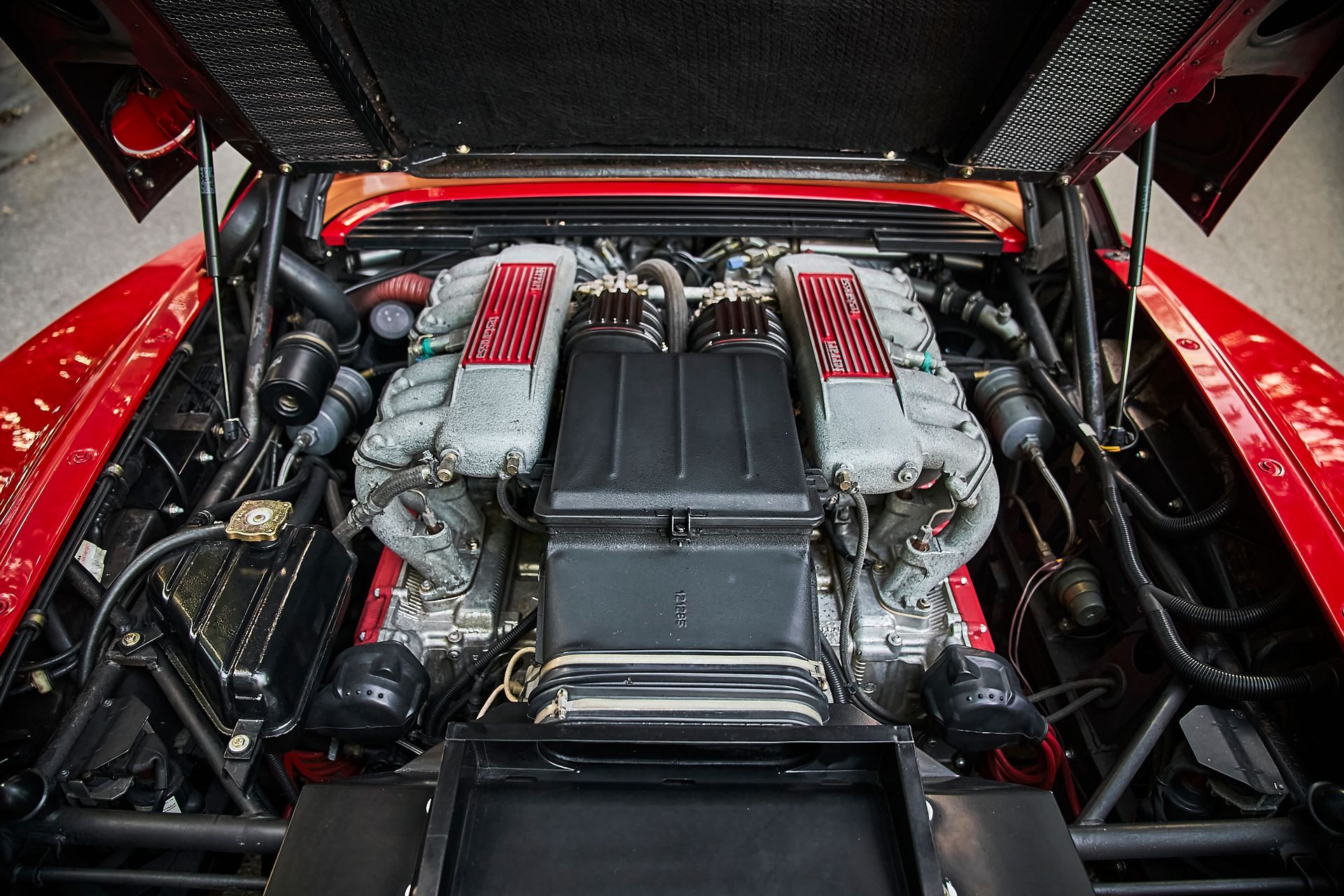 The engine of a red sports car with the hood up.