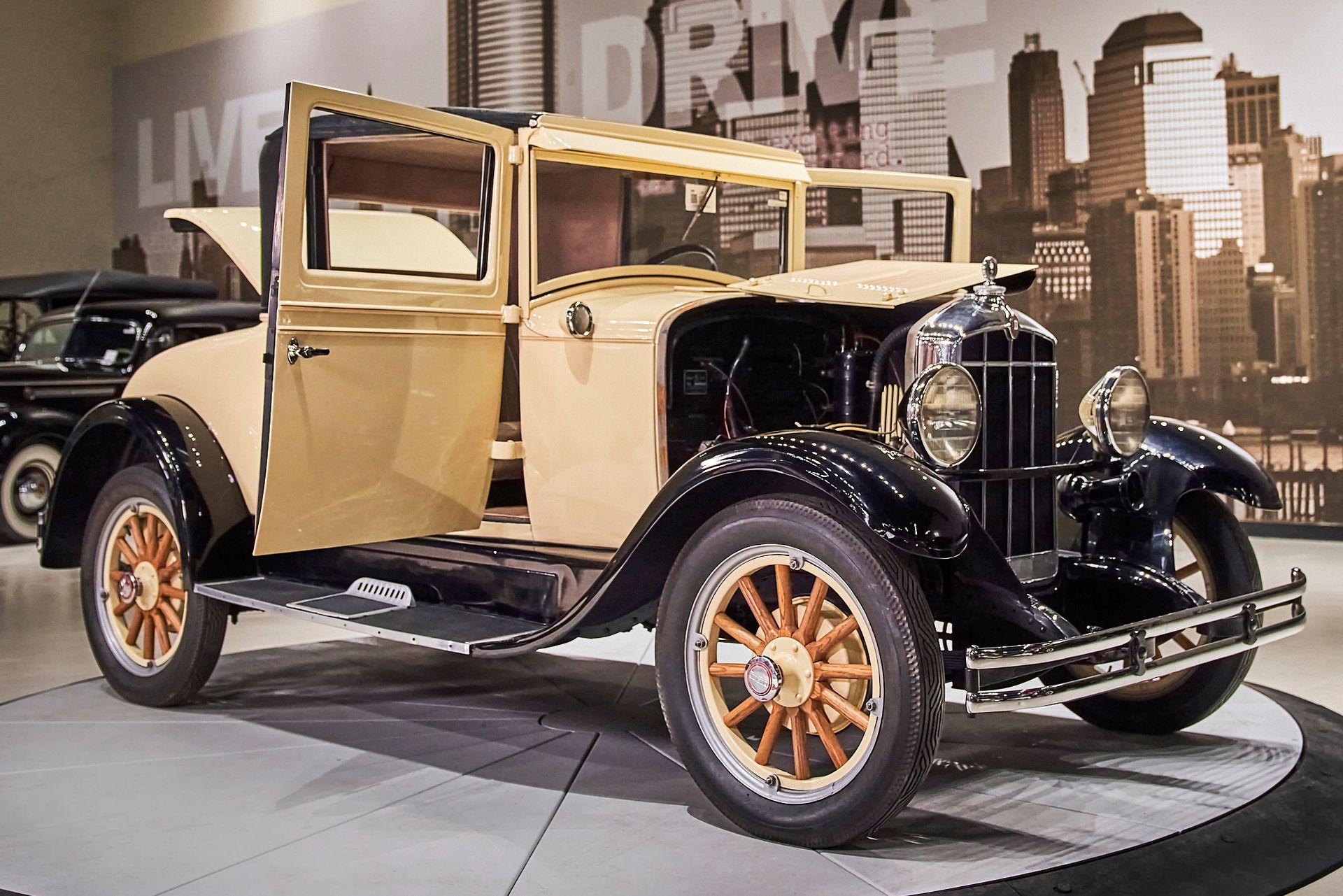 An old car is parked in front of a wall that says drive