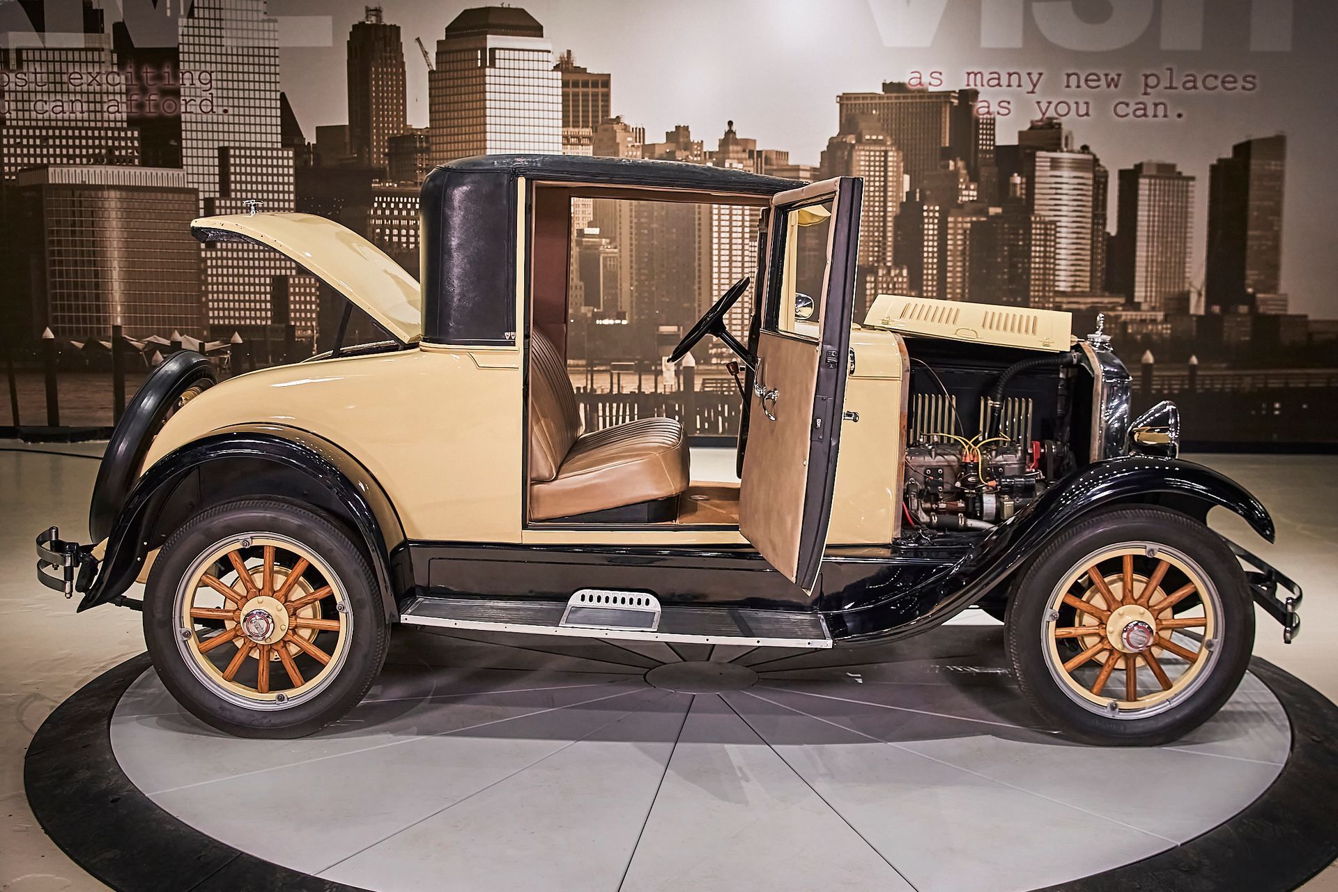 An old car with its doors open is on display in front of a city skyline.