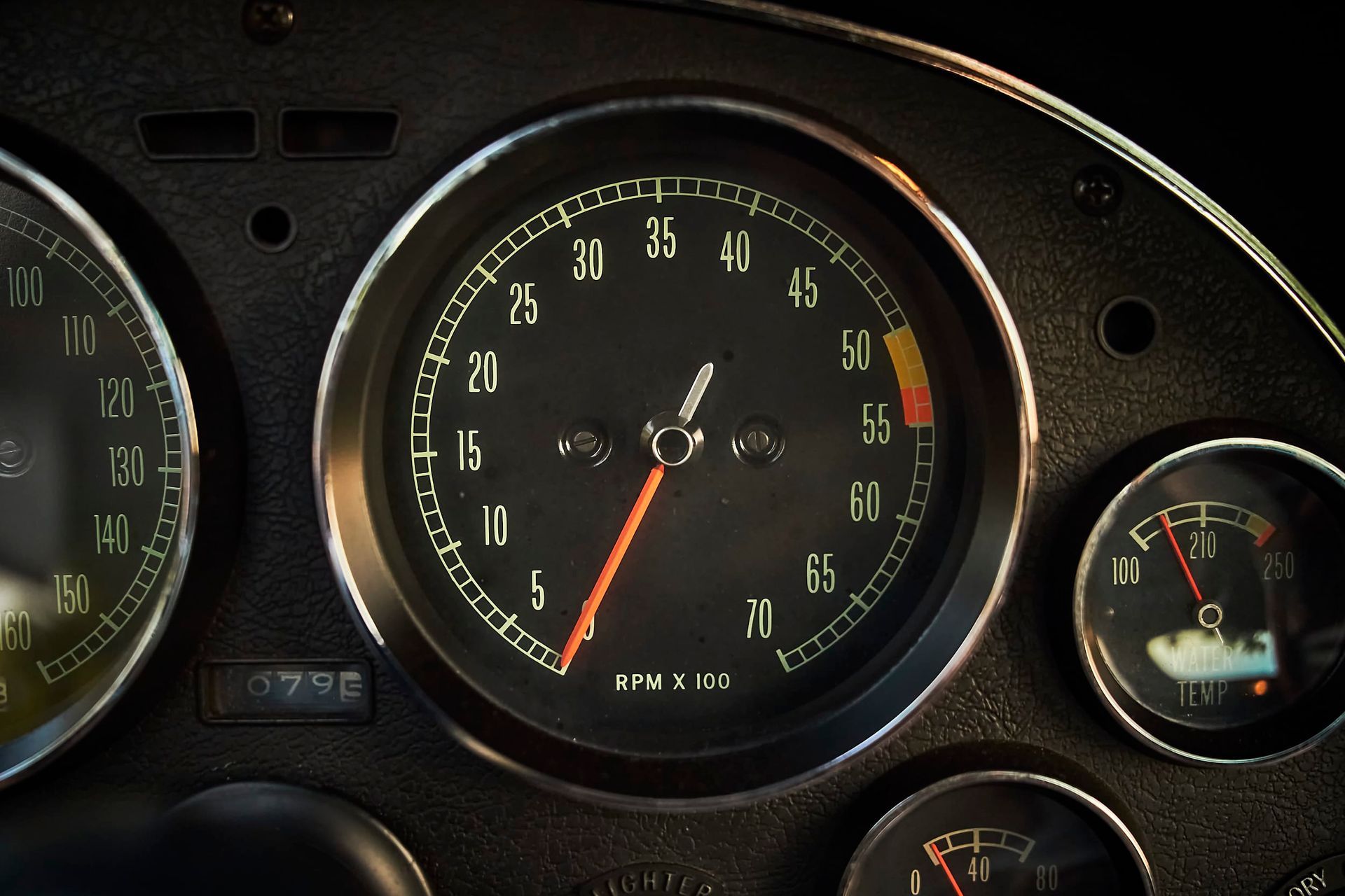 Dashboard of a car, close-up. The tachometer needle is at 5,000 RPM. Other gauges show speed and engine temperature.