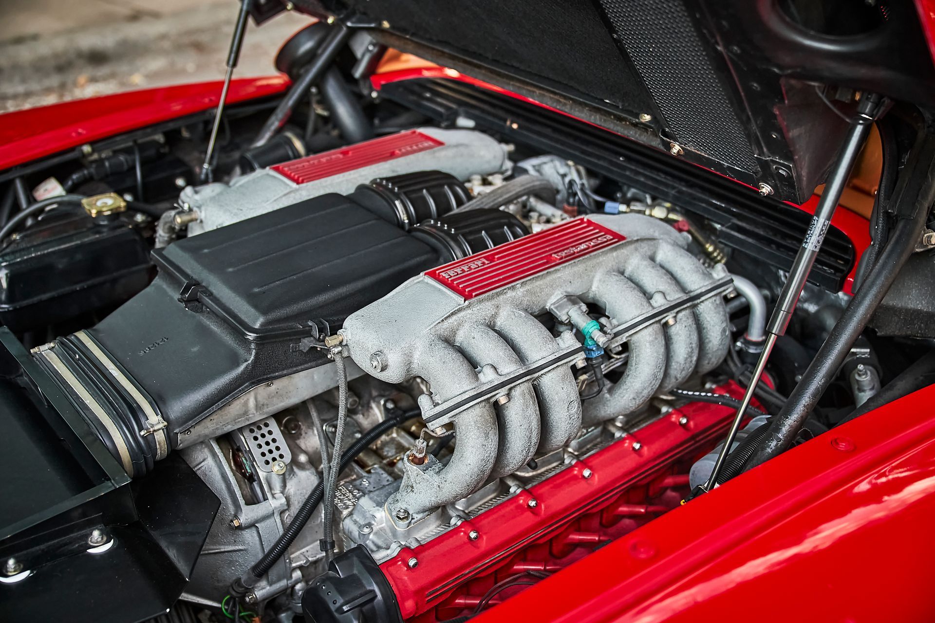 A close up of a red car engine with the hood open.