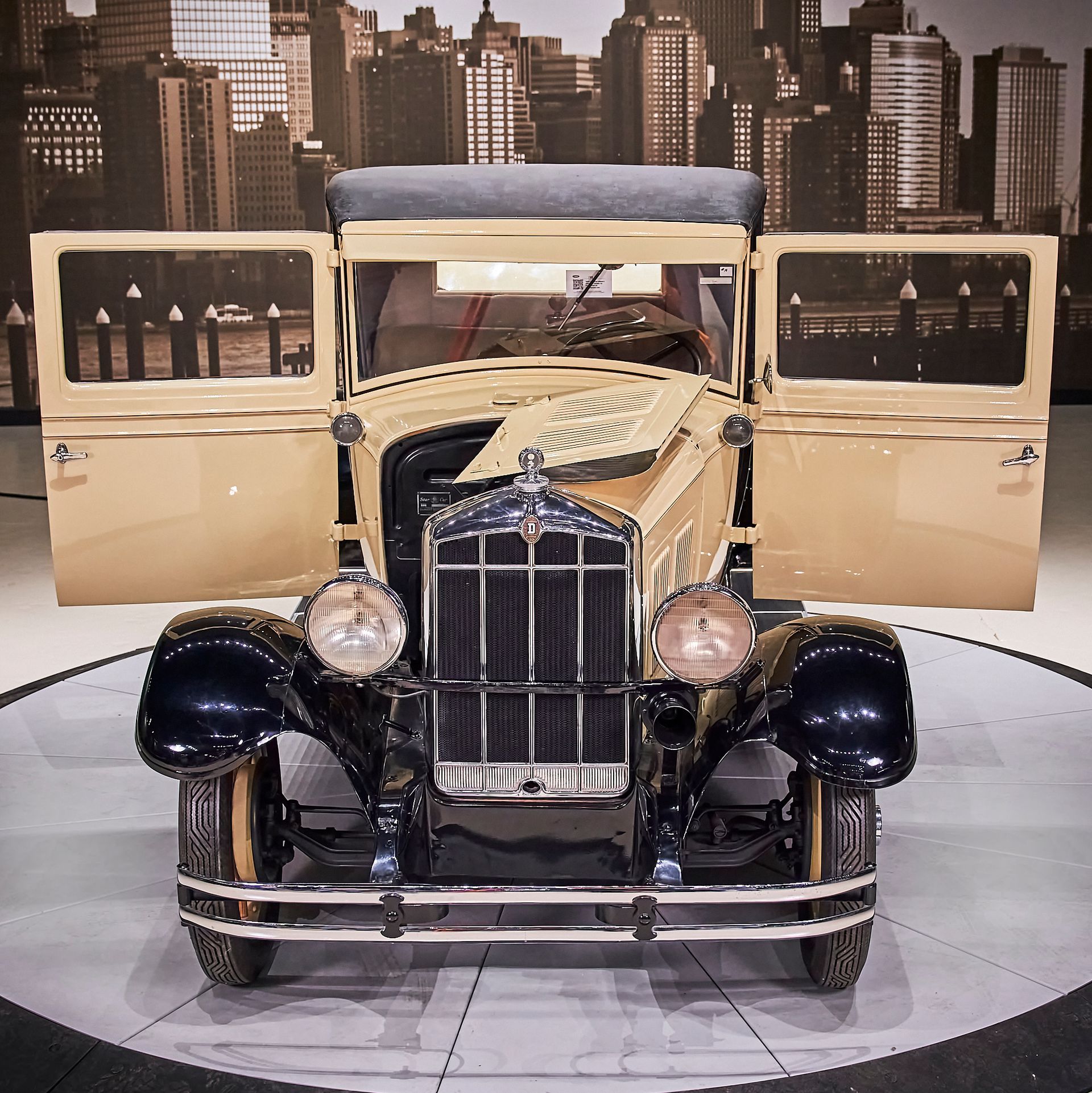 An old car with the doors open and a city in the background