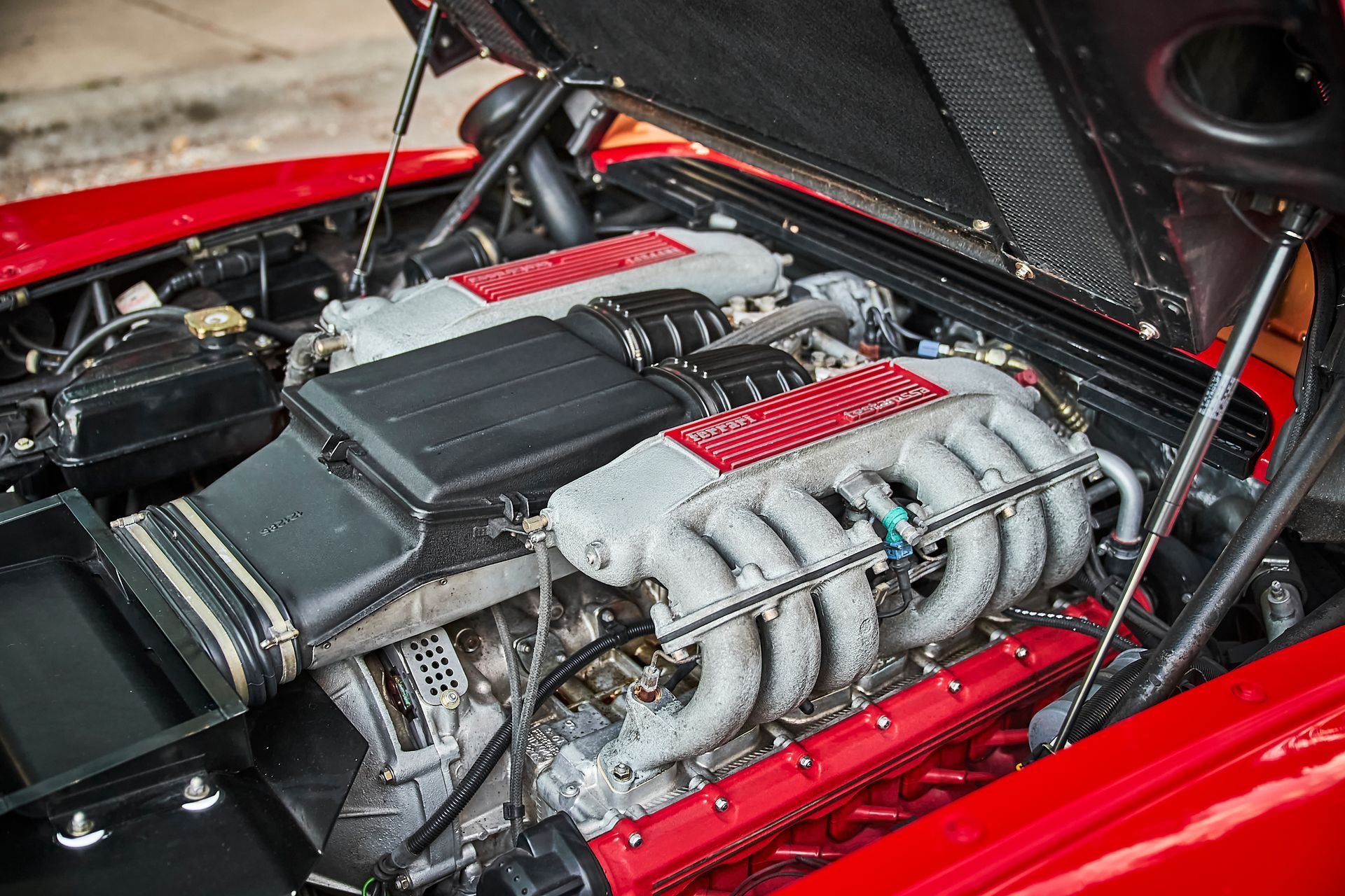 The engine of a red sports car with the hood open.