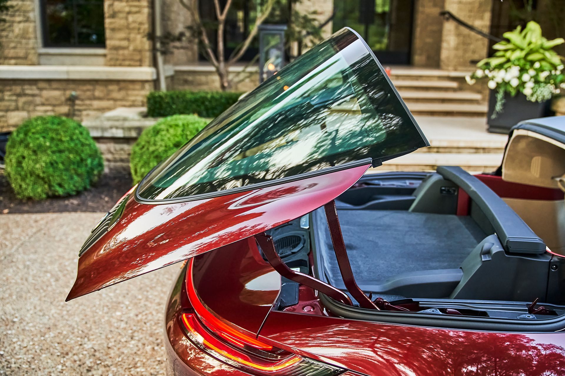 A red convertible car with the trunk open is parked in front of a house.