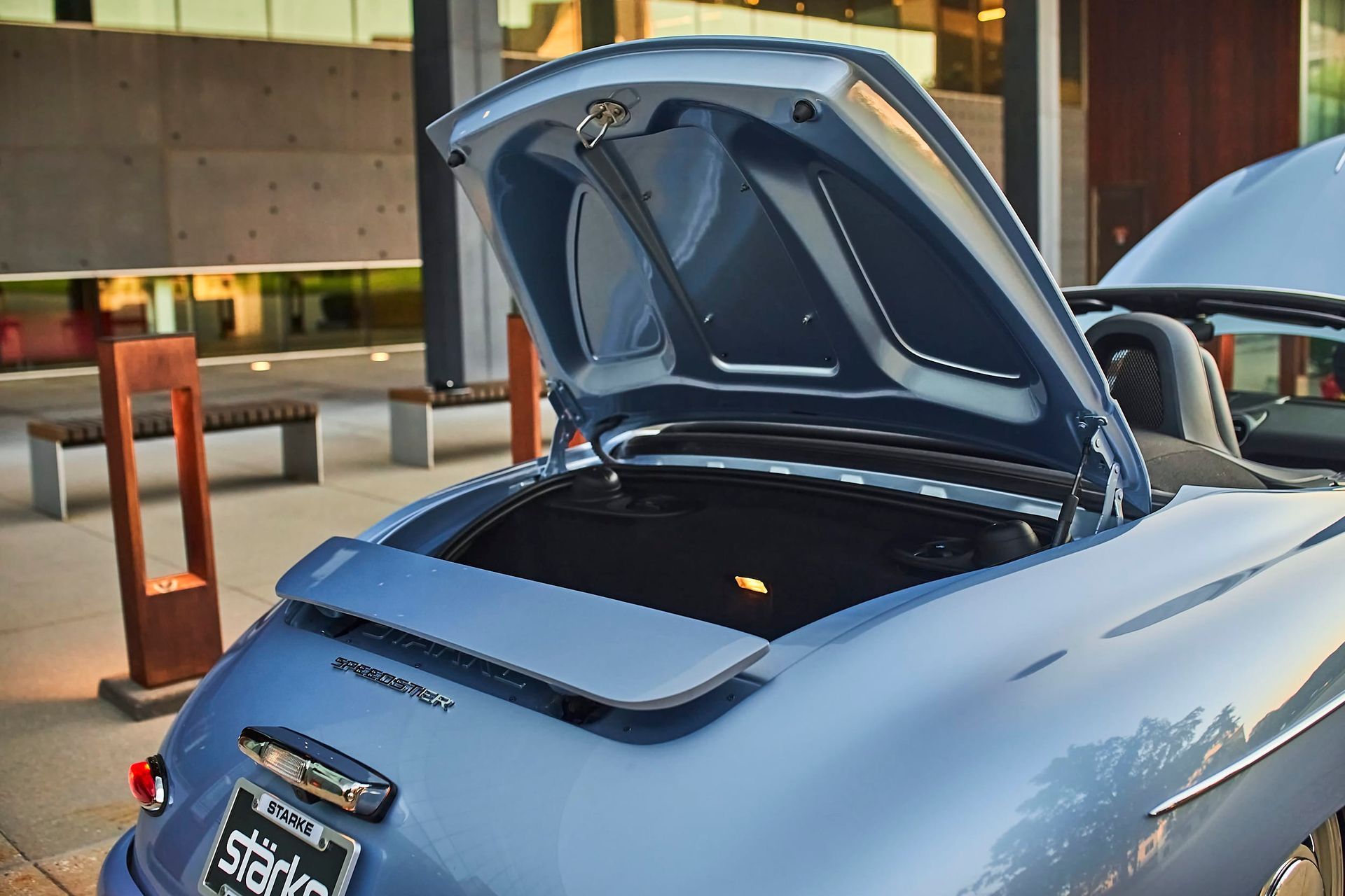 Light blue vintage Porsche convertible, trunk open, parked outside a building.