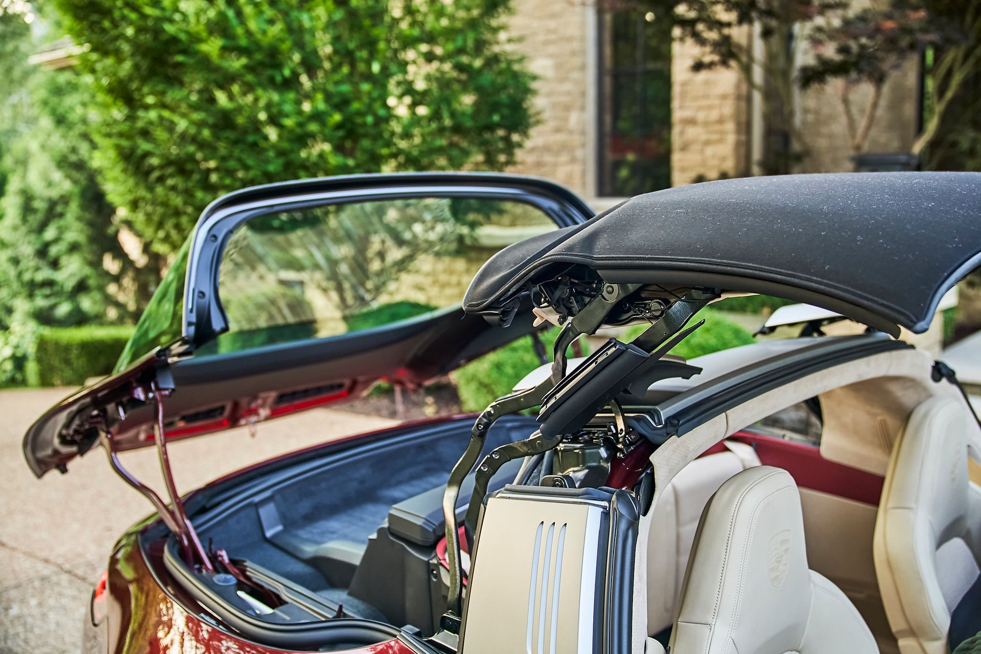 A red convertible car with the hood open is parked in front of a house.